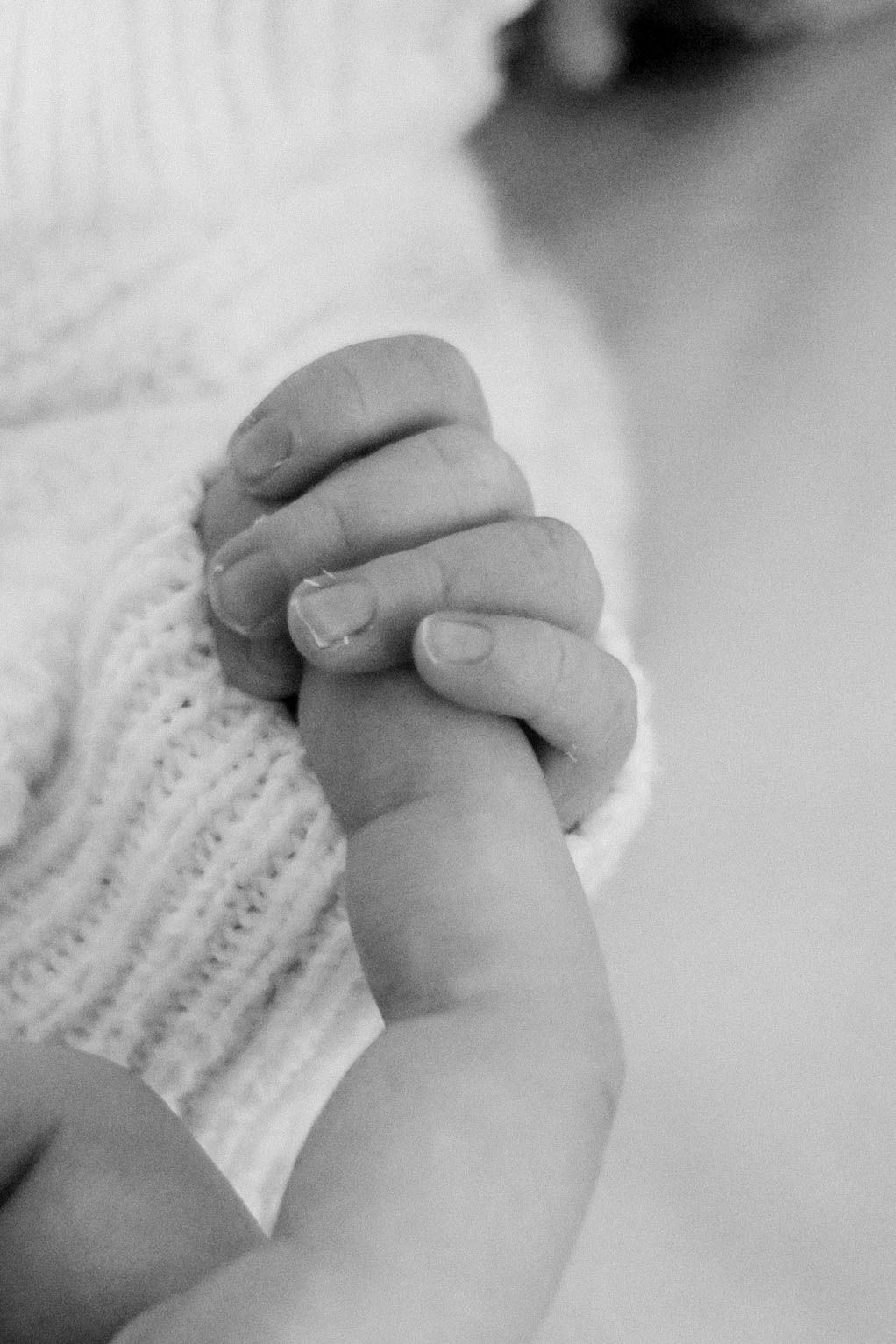 A black and white close-up of a baby gently holding an adult finger with tiny hands.