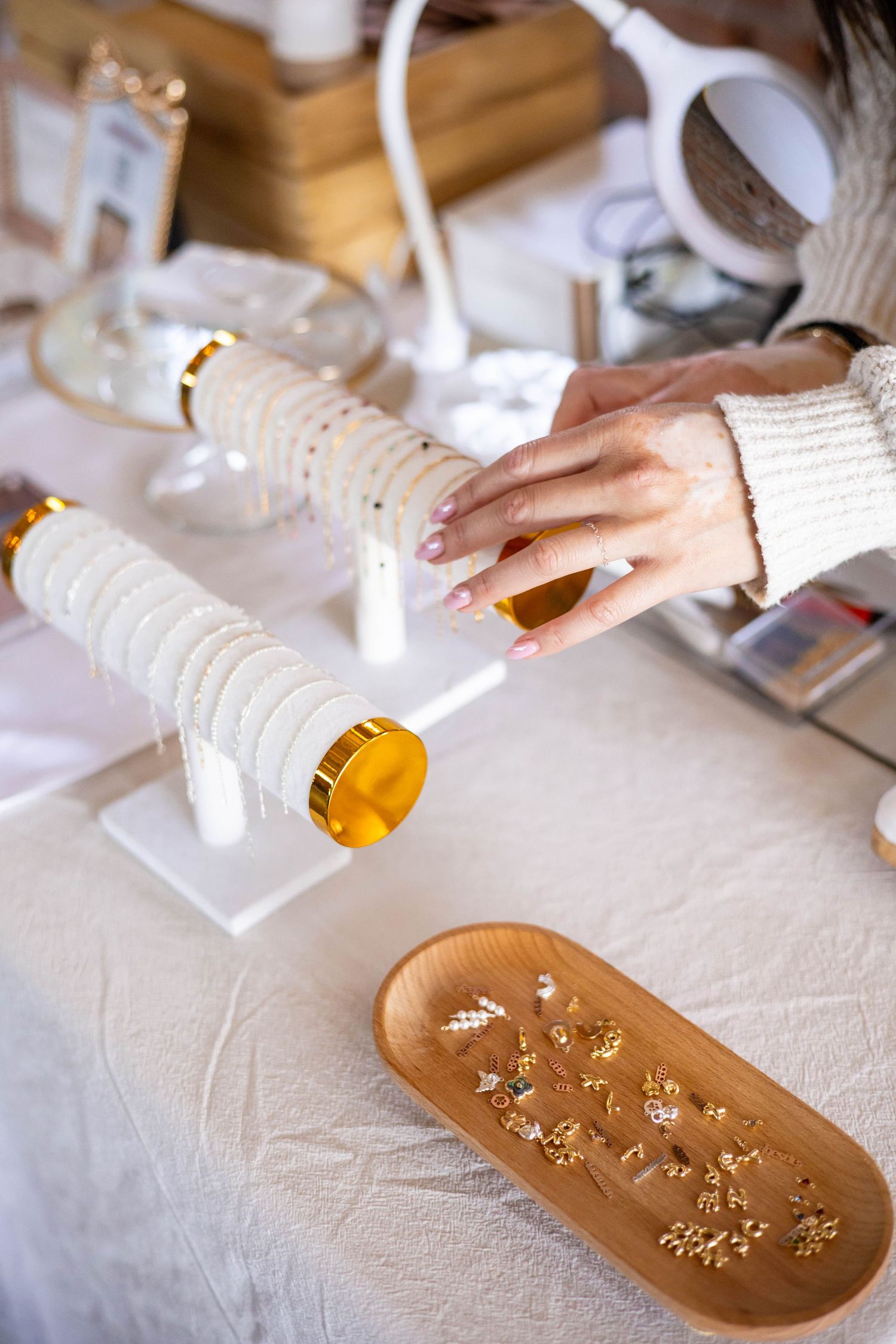 Woman browsing delicate gold jewelry displayed on white stands and wooden tray at a boutique jewelry shop.