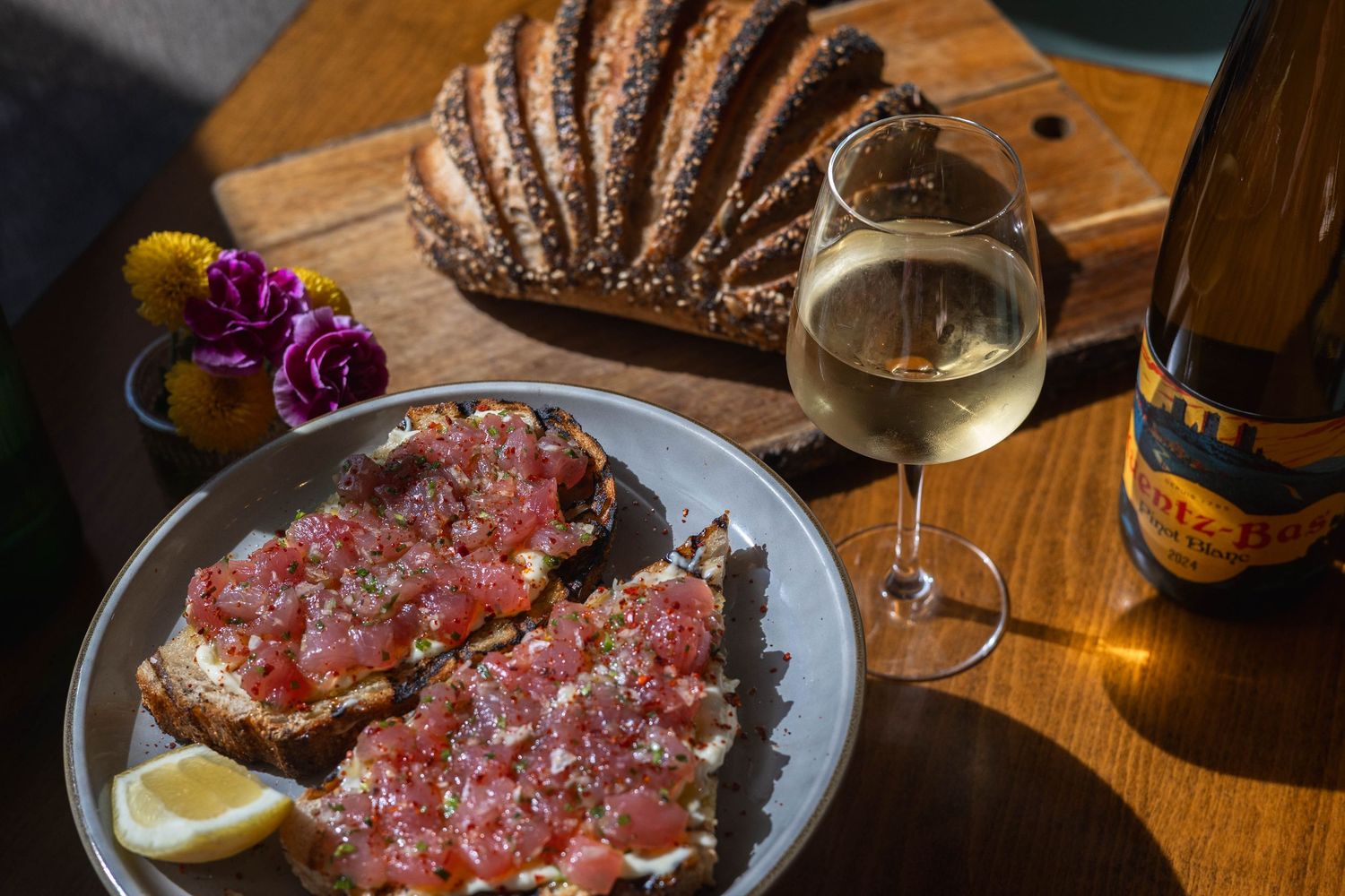 Smoked salmon on dark rye bread with lemon, served alongside a glass of white wine and a bottle on a wooden table.