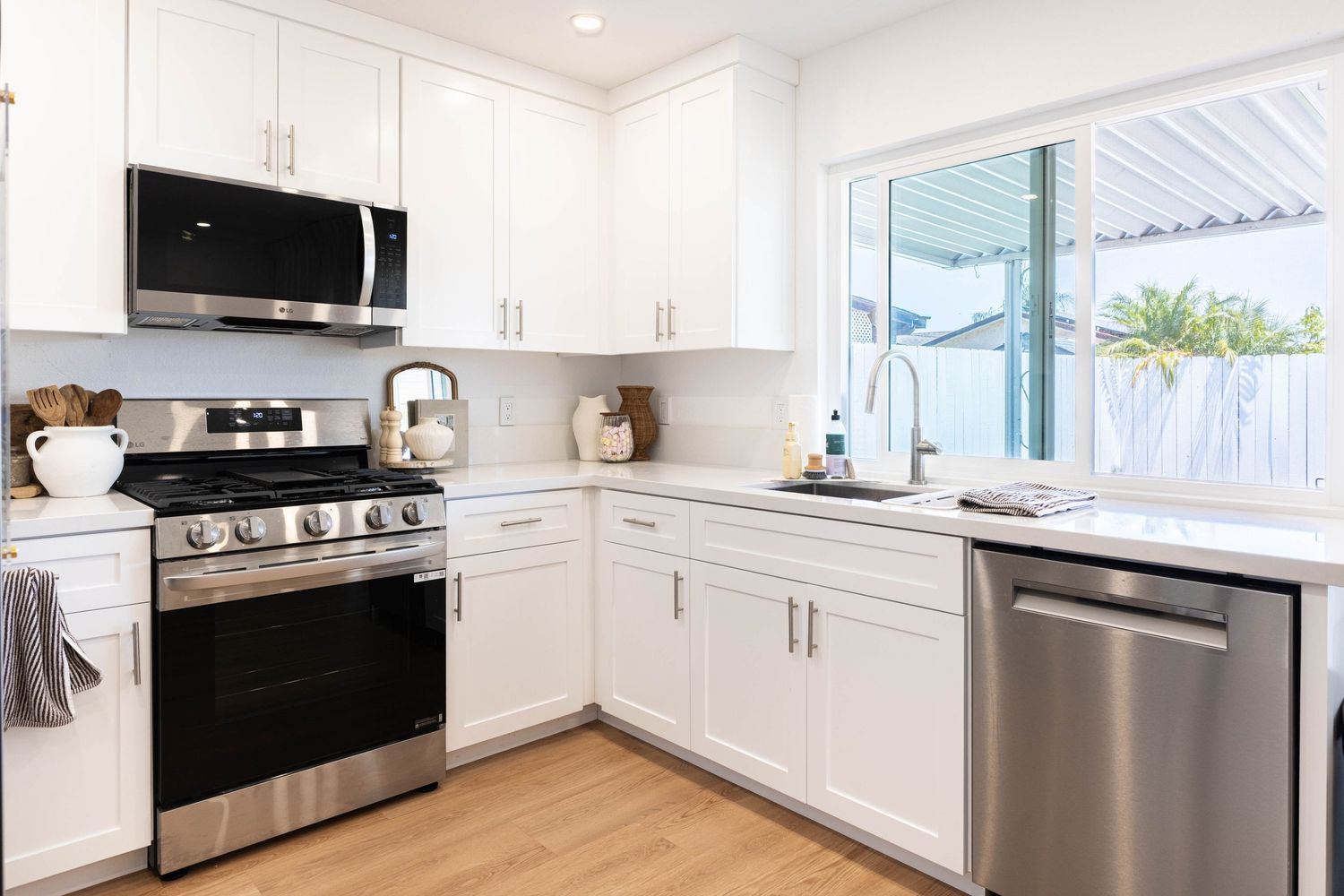 Modern white kitchen with stainless steel appliances, gas range, built-in microwave, dishwasher, and bright natural light.