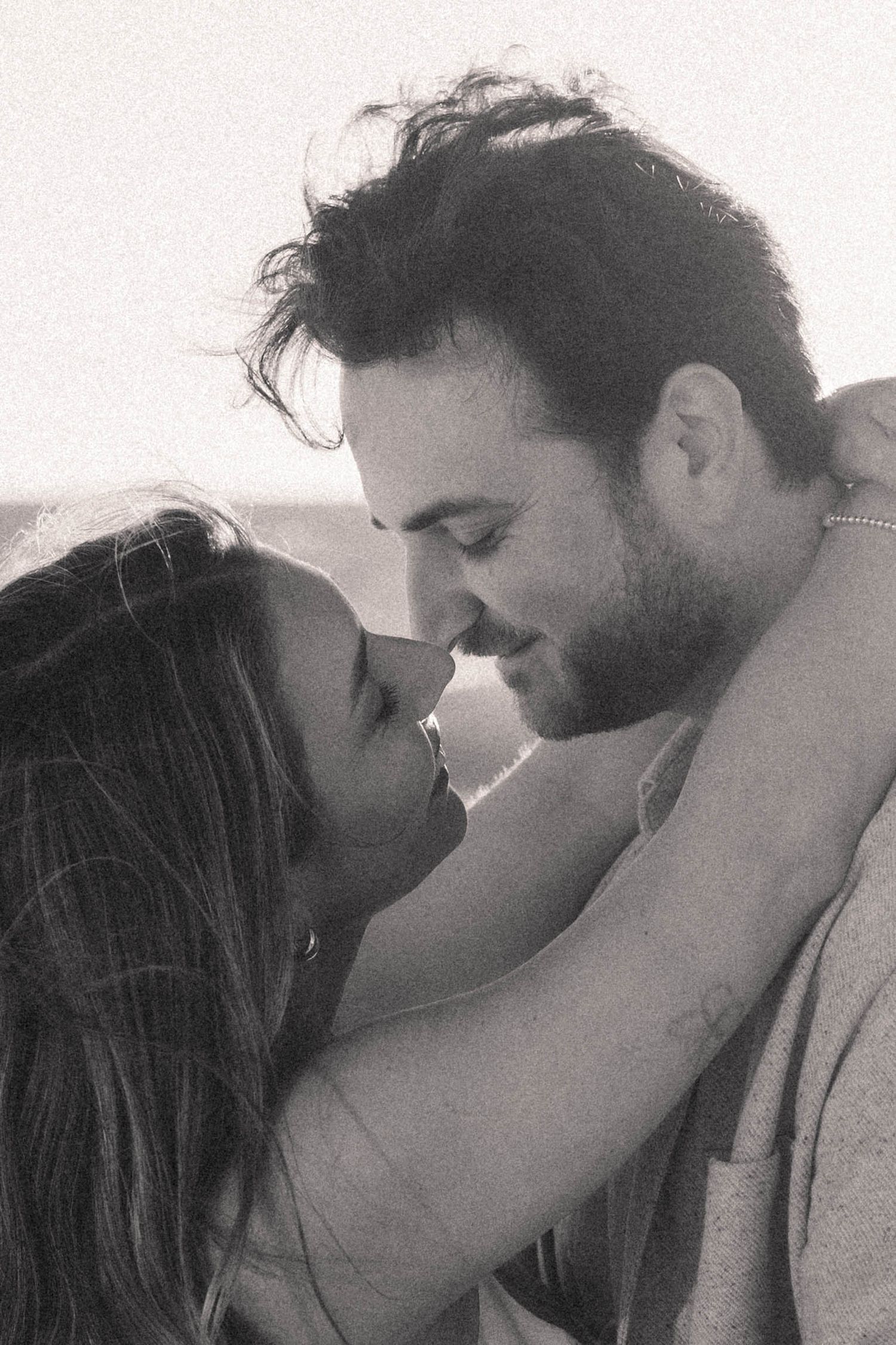 Black and white photo of a couple sharing an intimate moment about to kiss at the beach.