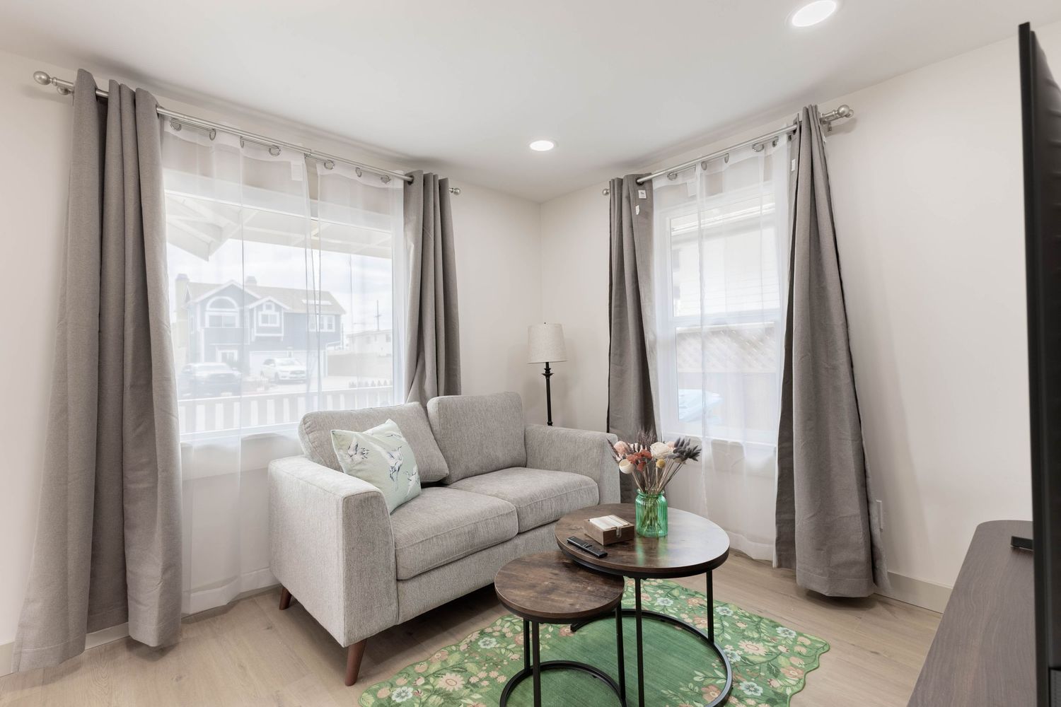 Bright living room with gray loveseat, round coffee table, green rug, and elegant gray curtains on hardwood floors.
