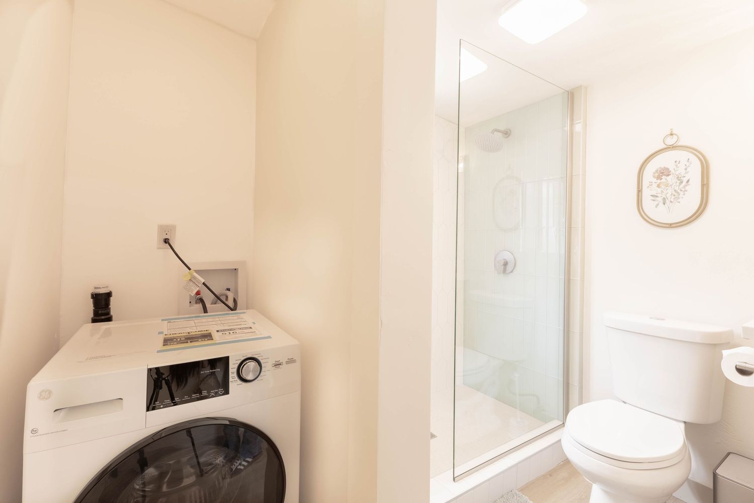 Compact laundry area with washer next to a glass shower stall and toilet in a small bathroom.