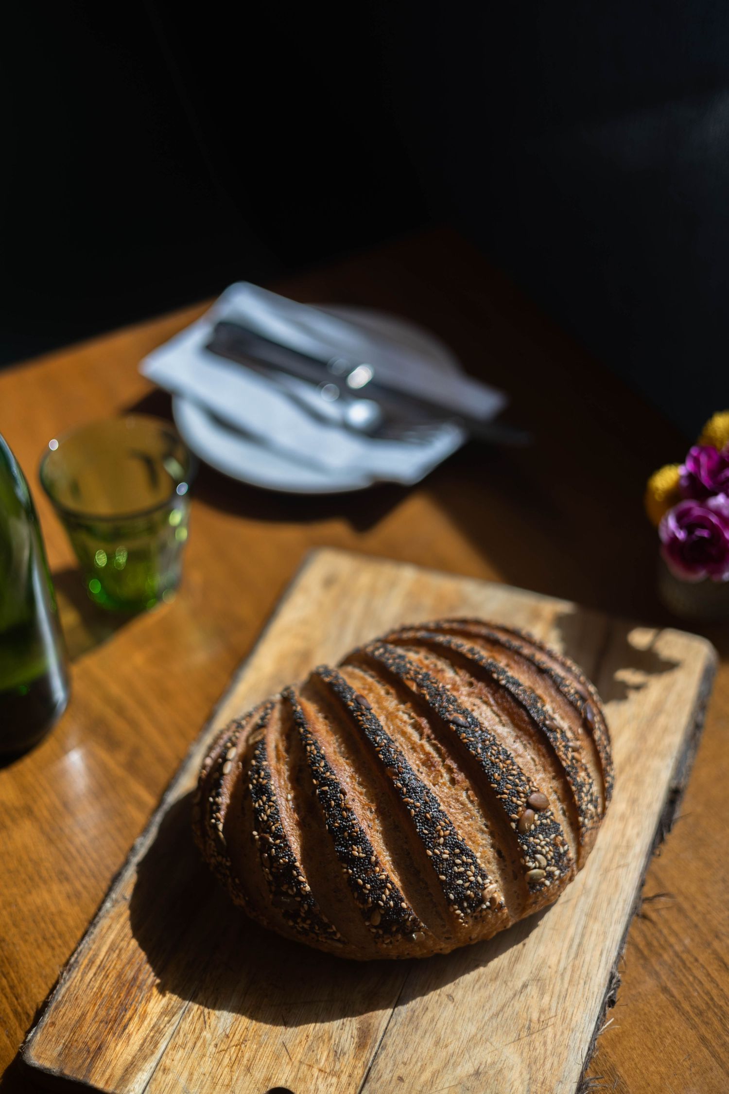 Freshly baked dark rye bread loaf with poppy seeds on a wooden cutting board in a restaurant setting.