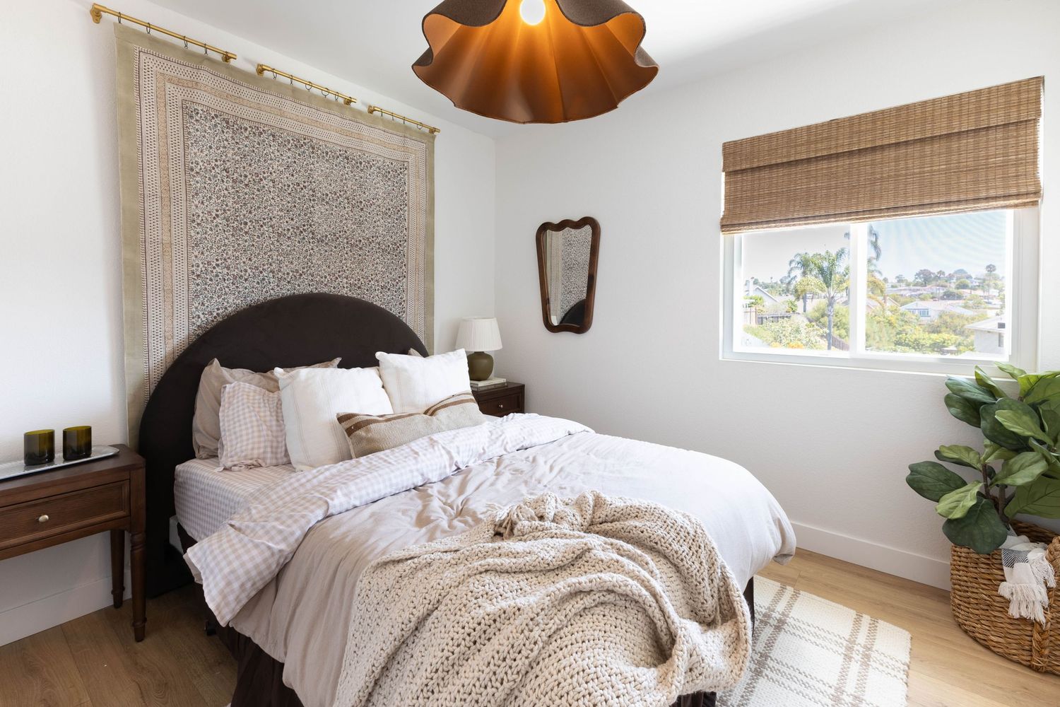 Cozy bedroom with dark wood bed, white bedding, chunky knit throw, bamboo shade window, and boho wall tapestry.