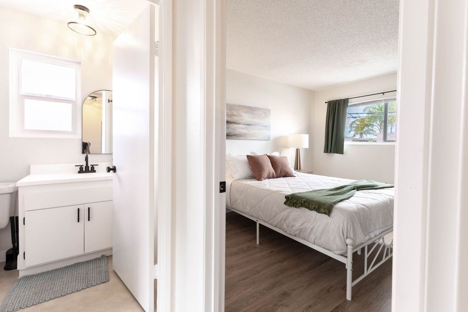 Bright bedroom with white metal bed frame and en-suite bathroom featuring white vanity and mirror.