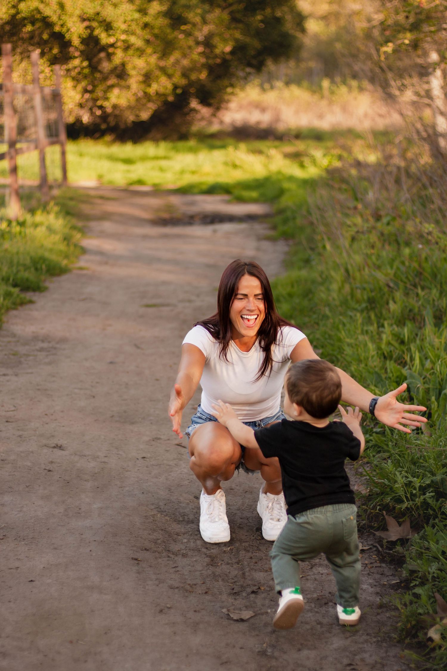 Joyful mother crouching on a dirt path as her toddler runs toward her with open arms.