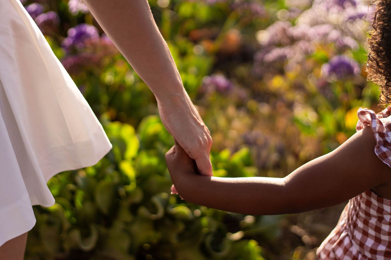 Close-up of a mother and young daughter holding hands among colorful garden flowers.