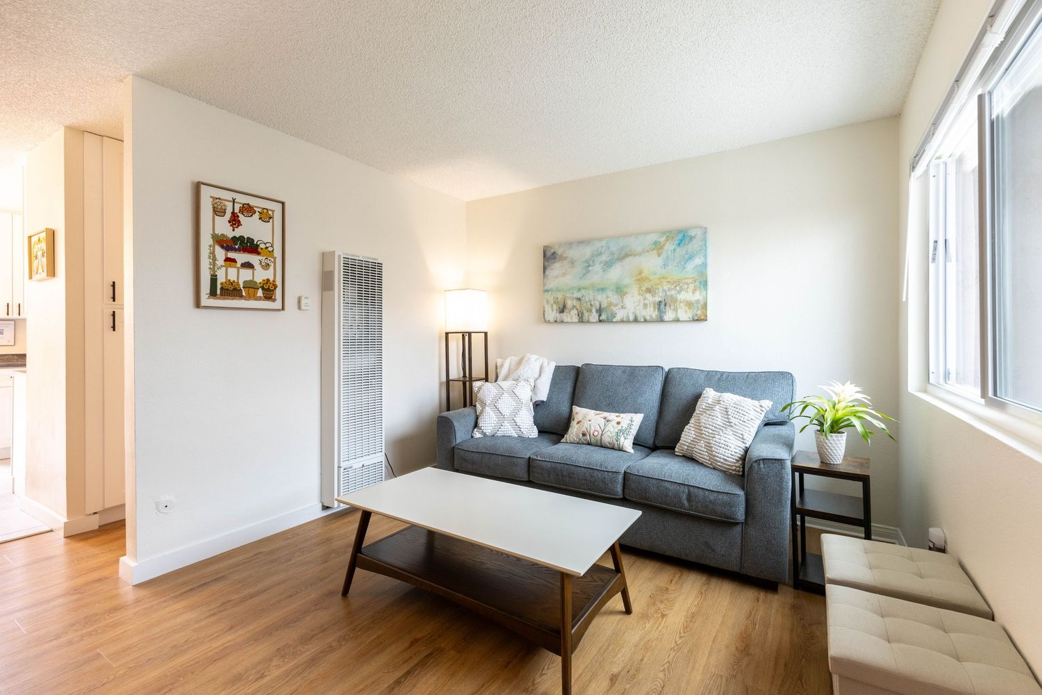 Modern living room with gray sofa, wood floors, coffee table, and bright windows in a cozy apartment.