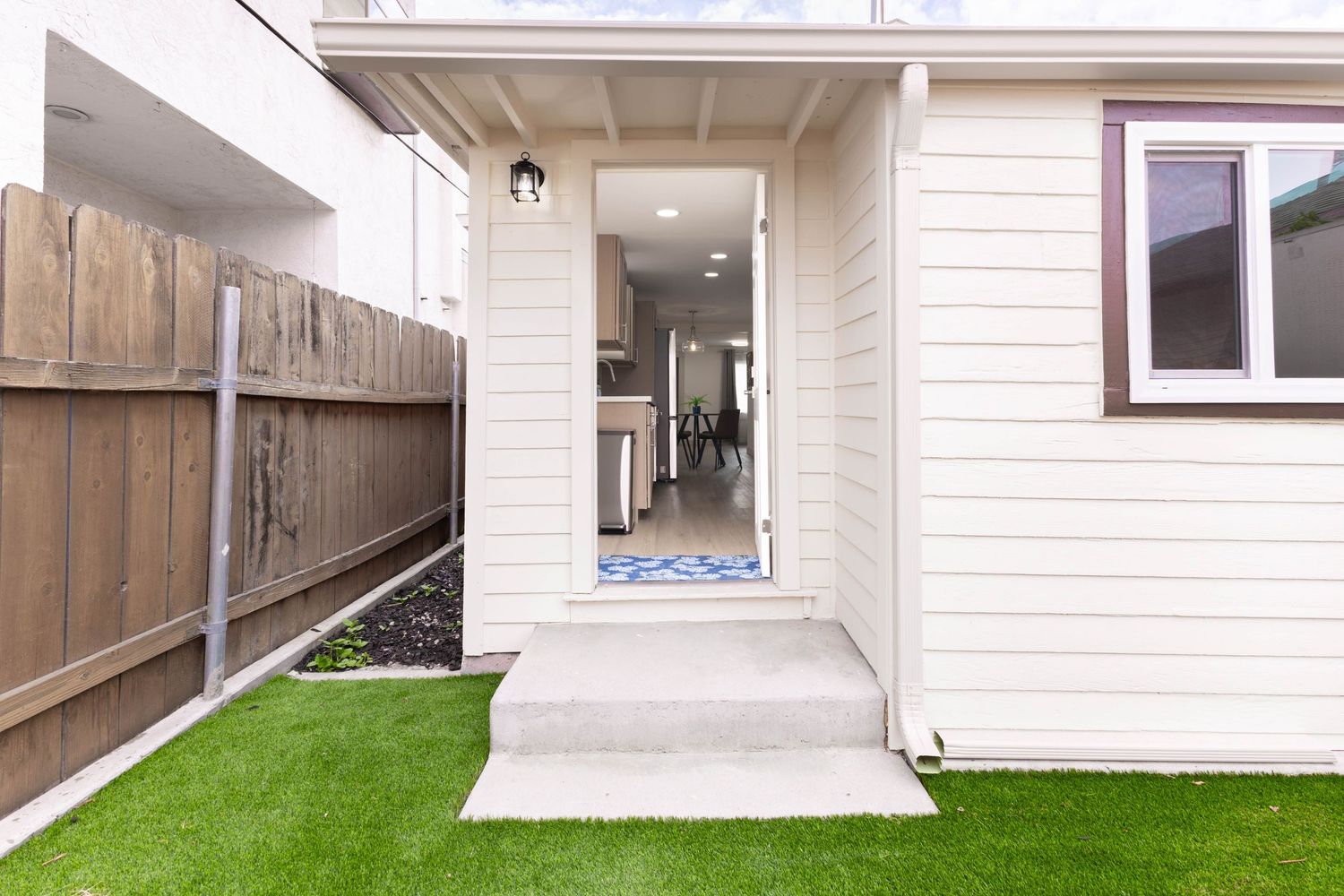White home exterior with green lawn, wood fence, and open entry door.