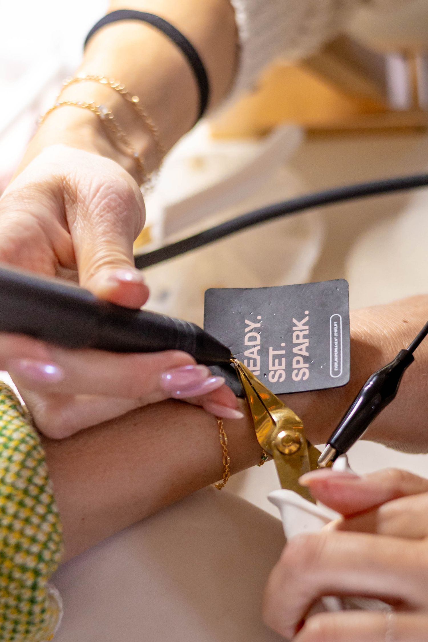Close-up of jewelry engraving service with a Ready Set Spark branded card and gold bracelet being personalized.