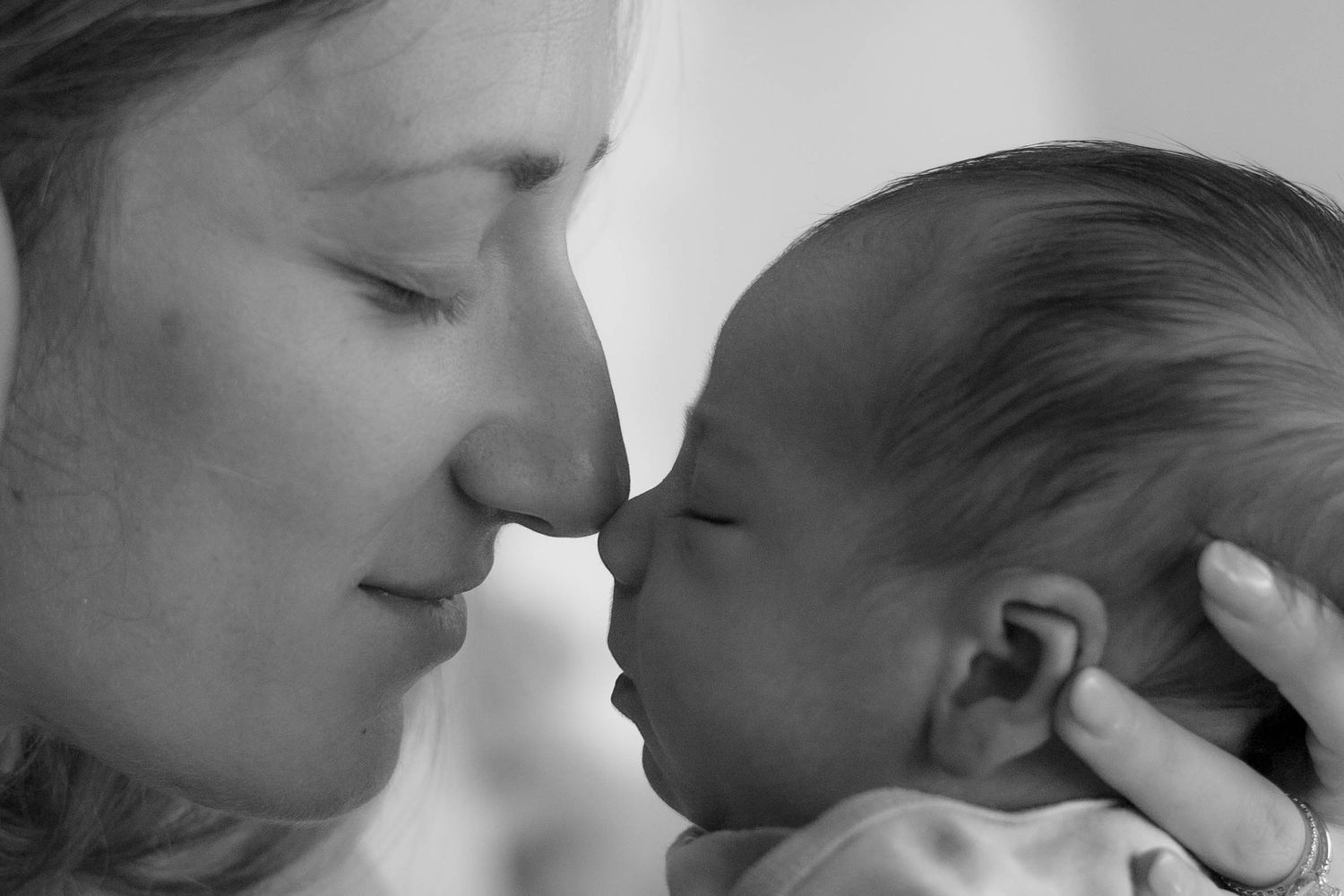 A mother and newborn baby share a tender nose-to-nose moment in an intimate black and white portrait.