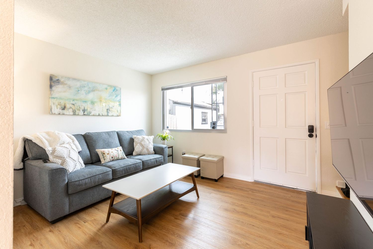 Modern living room with gray sofa, wood coffee table, hardwood floors, and bright window in a cozy apartment.