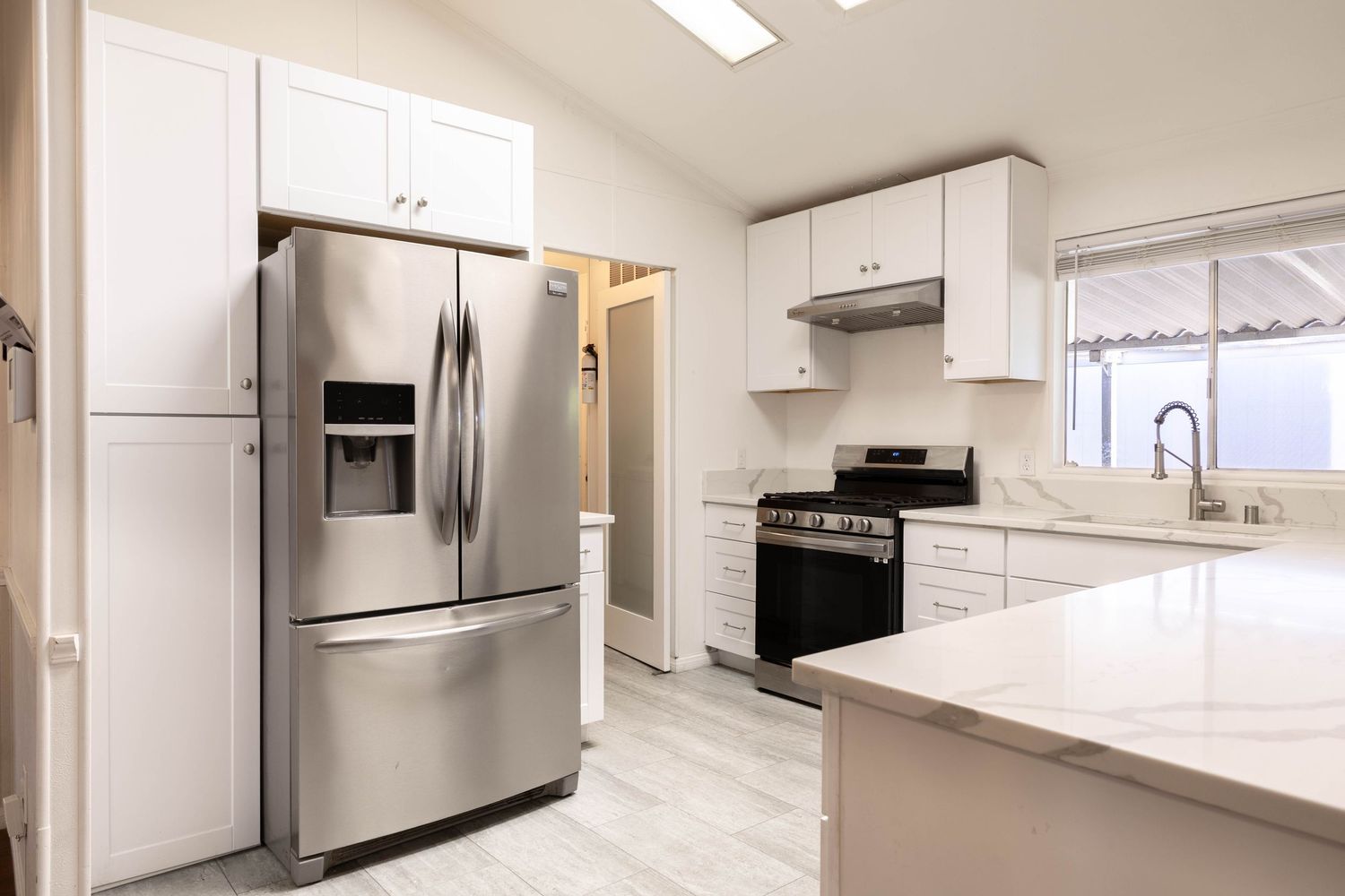 Modern kitchen with stainless steel French door refrigerator, gas range, white cabinets, and marble countertops.