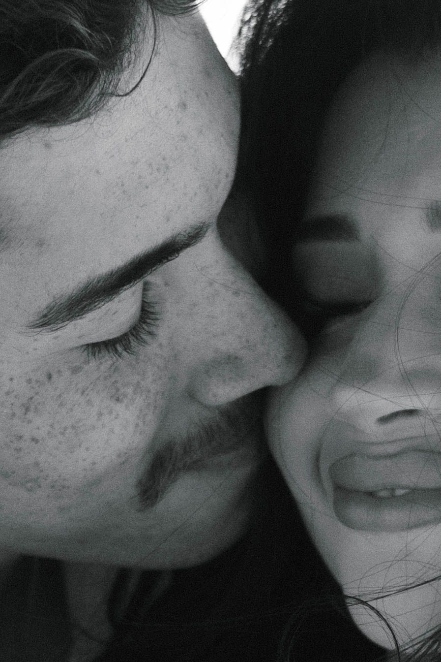 Black and white close-up of couple sharing tender moment, man with freckles kissing womans cheek.