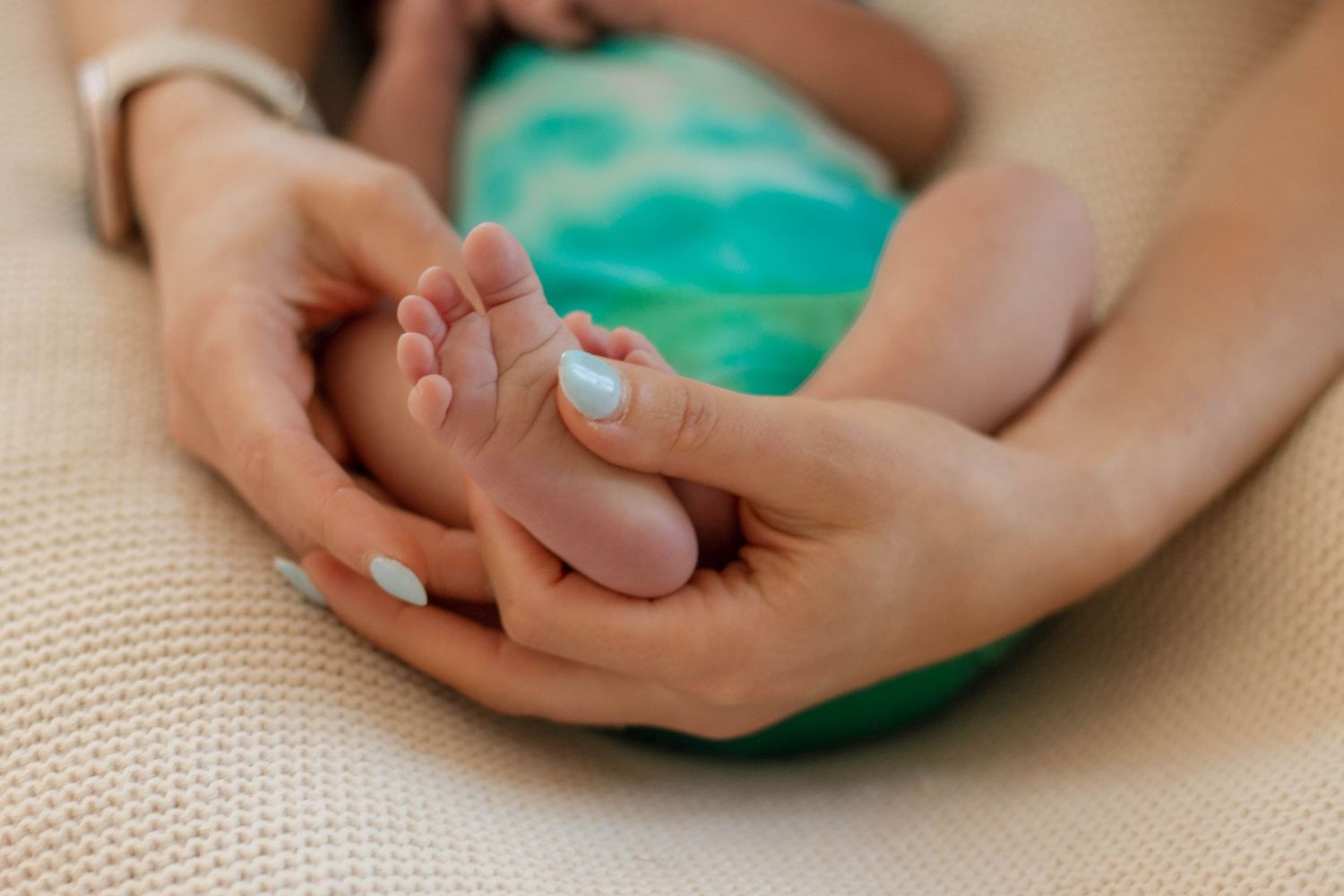 Close-up of tiny newborn baby feet gently held in parents hands on soft blanket.