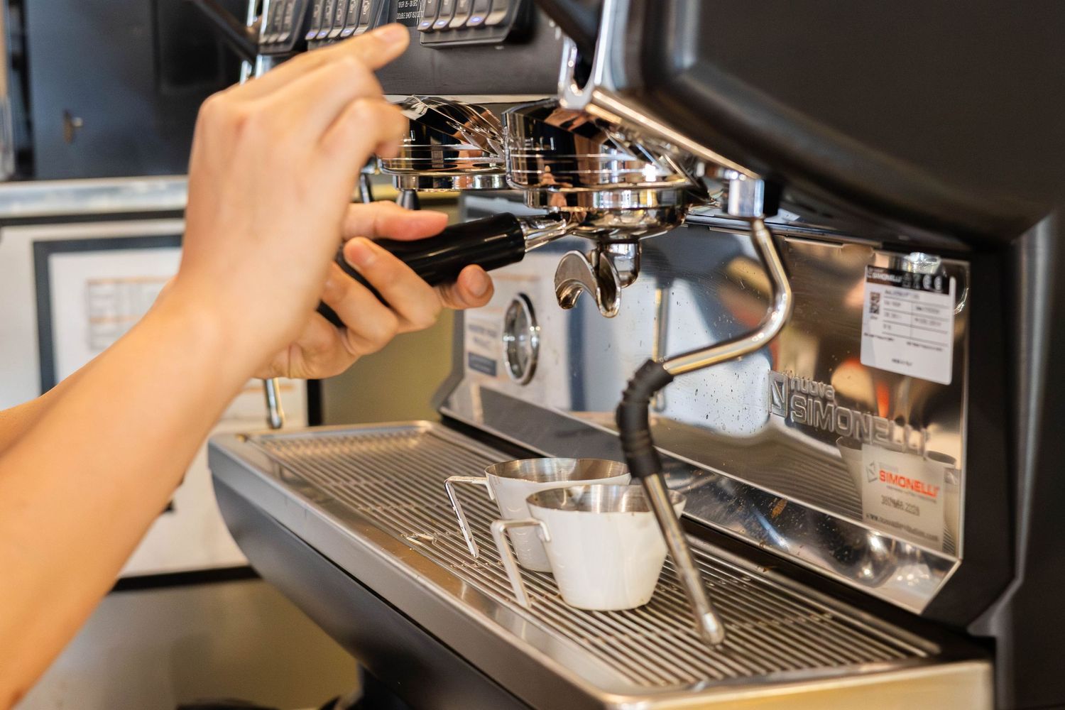 Barista operating a professional espresso machine, steaming milk in a white cup at a coffee shop.