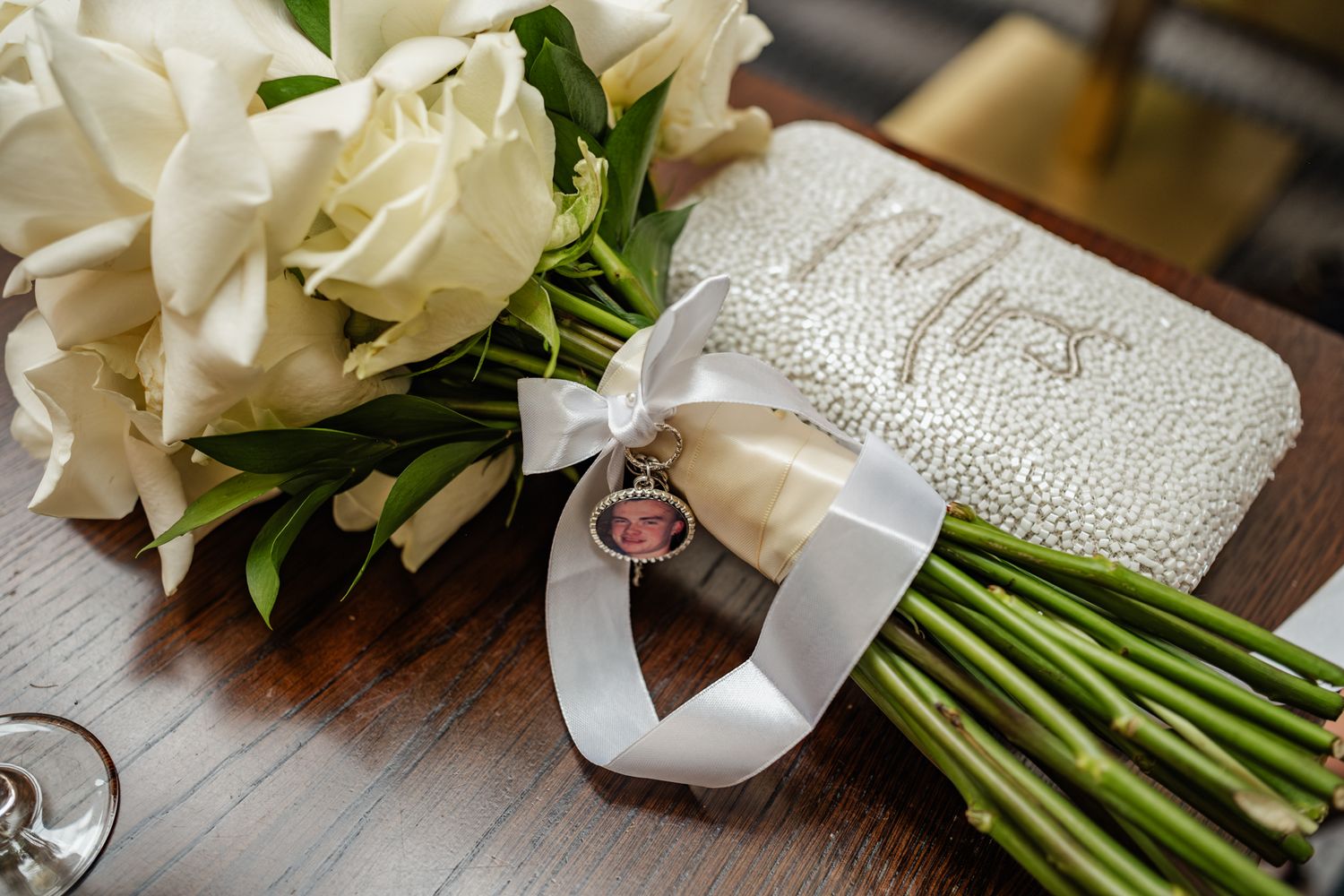 Elegant white rose wedding bouquet with satin ribbon and memorial charm.