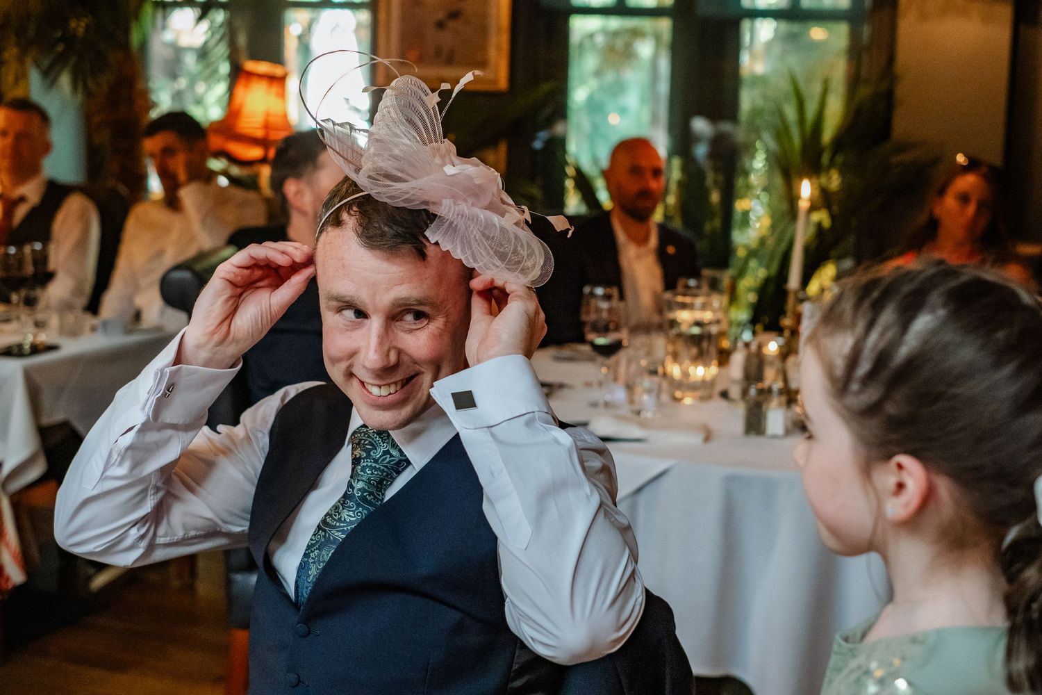 Guest trying on a whimsical feathered hat during wedding reception celebrations.