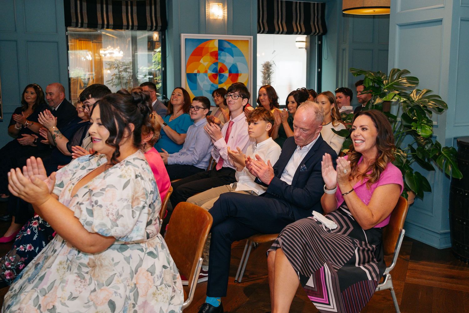 Wedding guests enjoying a celebration in a room with teal walls and large windows.