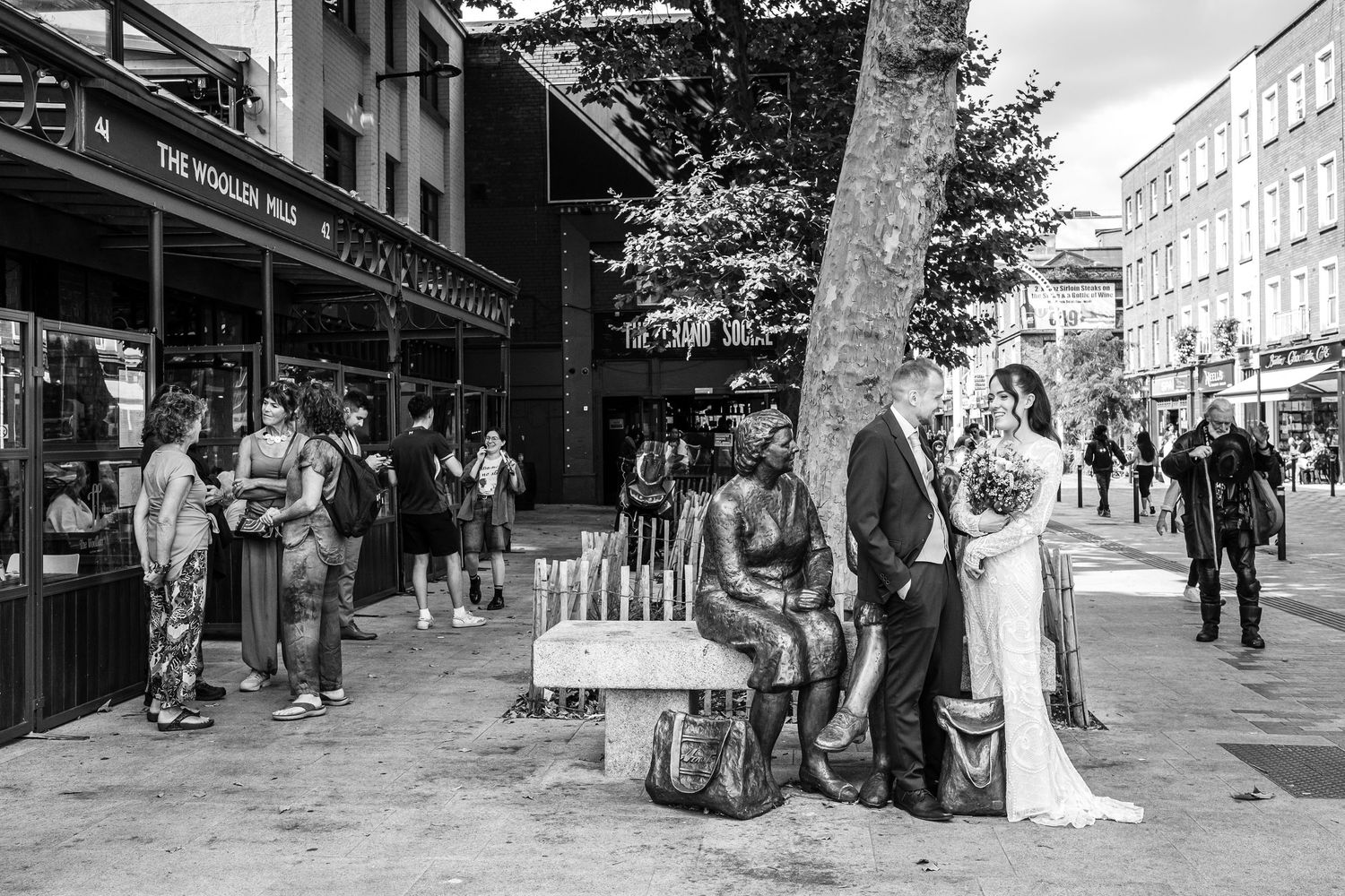 Black and white street photography of wedding party walking among urban crowds.