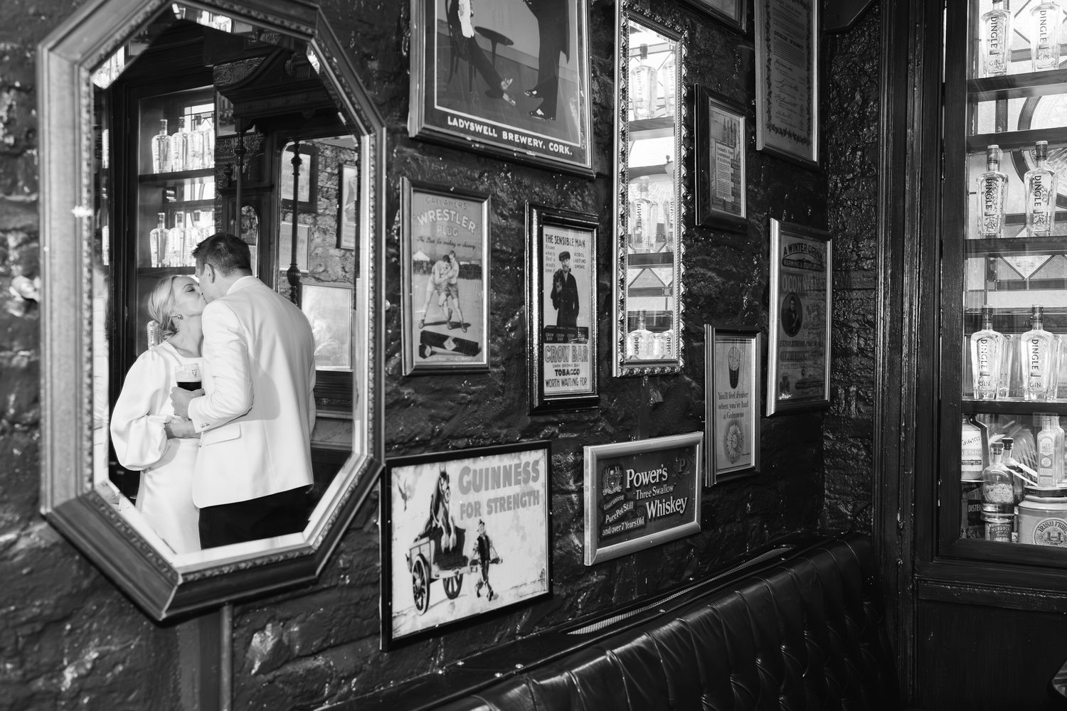 Black and white photo of a couple embracing in a pub with Guinness and Powers Whiskey vintage signs on the wall.