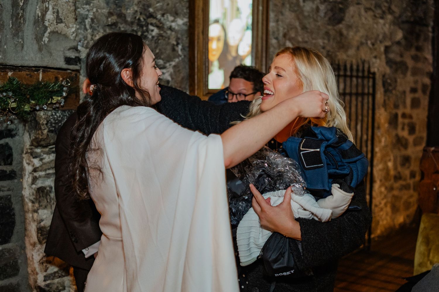Two women embracing warmly in a rustic stone venue, sharing a joyful reunion moment.