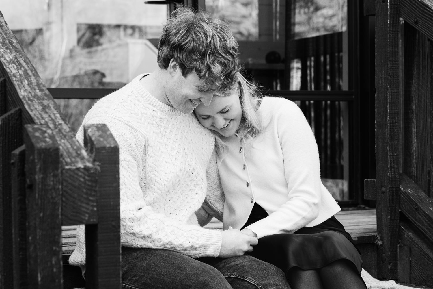 A candid black and white moment showing two people sharing laughter while sitting together outdoors.