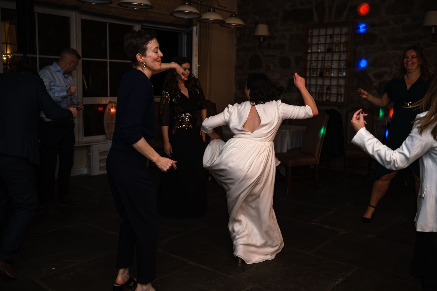 Bride in white dress dancing joyfully with guests at a lively wedding reception party.