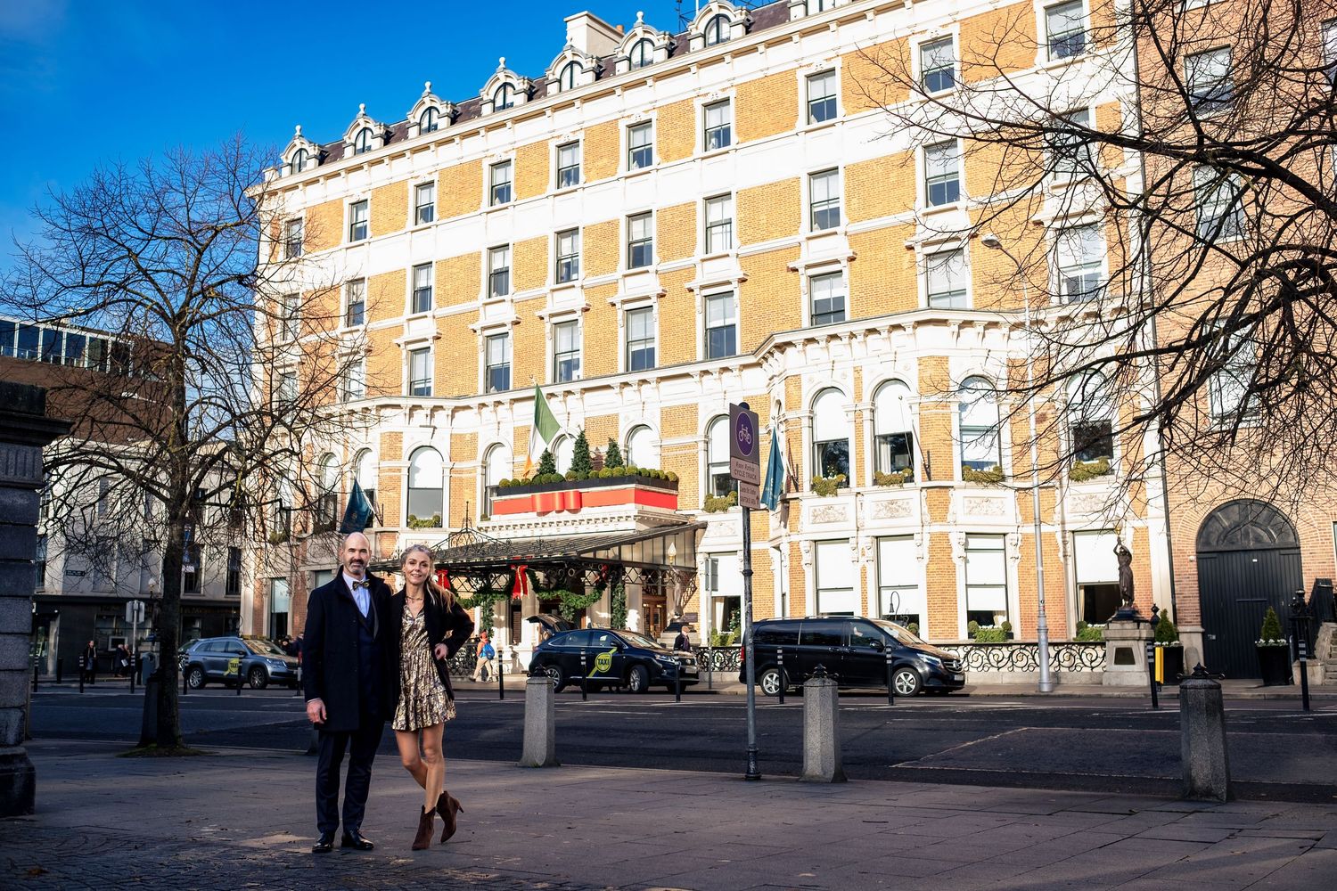 Couple standing in front of a grand historic hotel building on a sunny day.