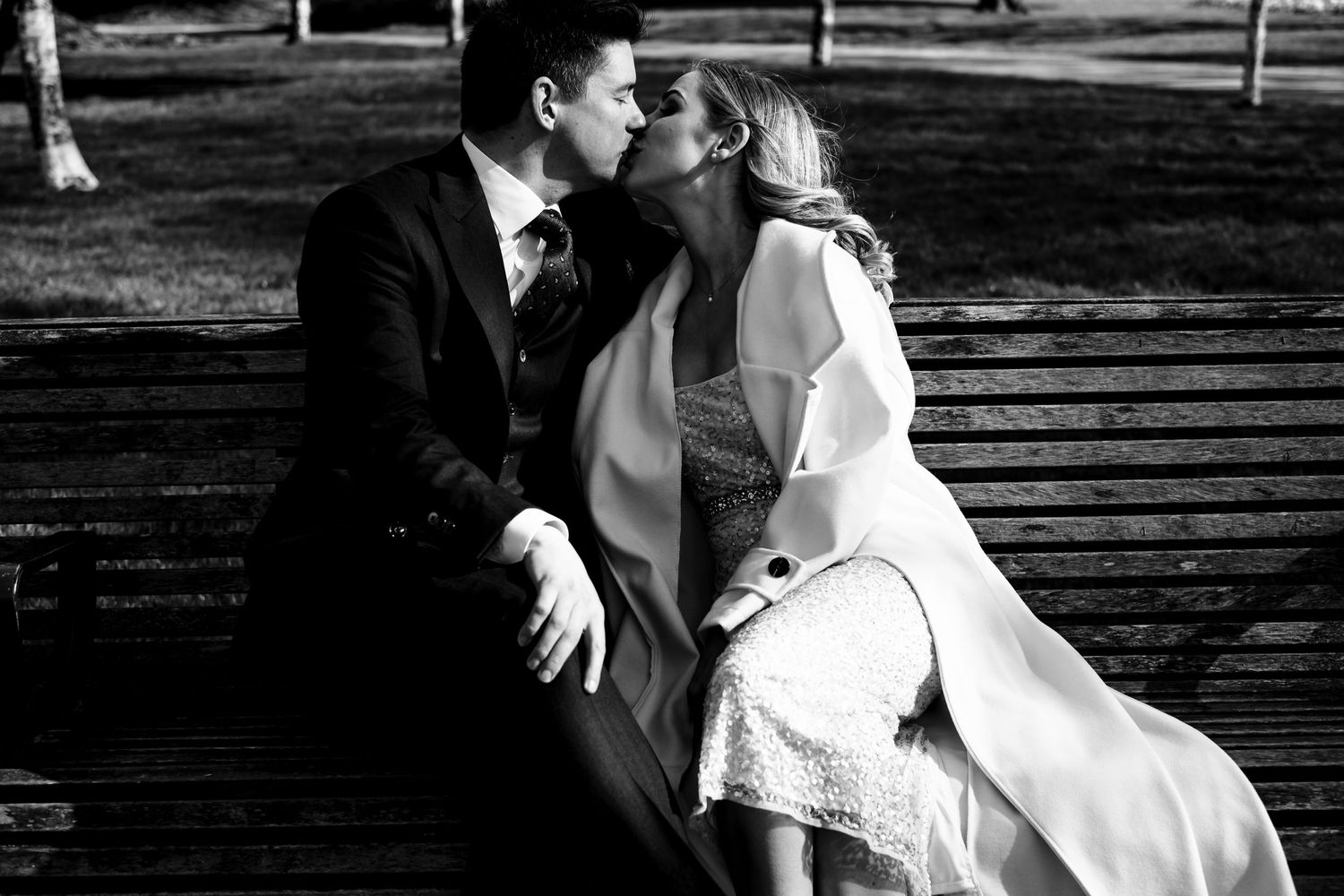 Black and white photo of couple sharing romantic moment on park bench.