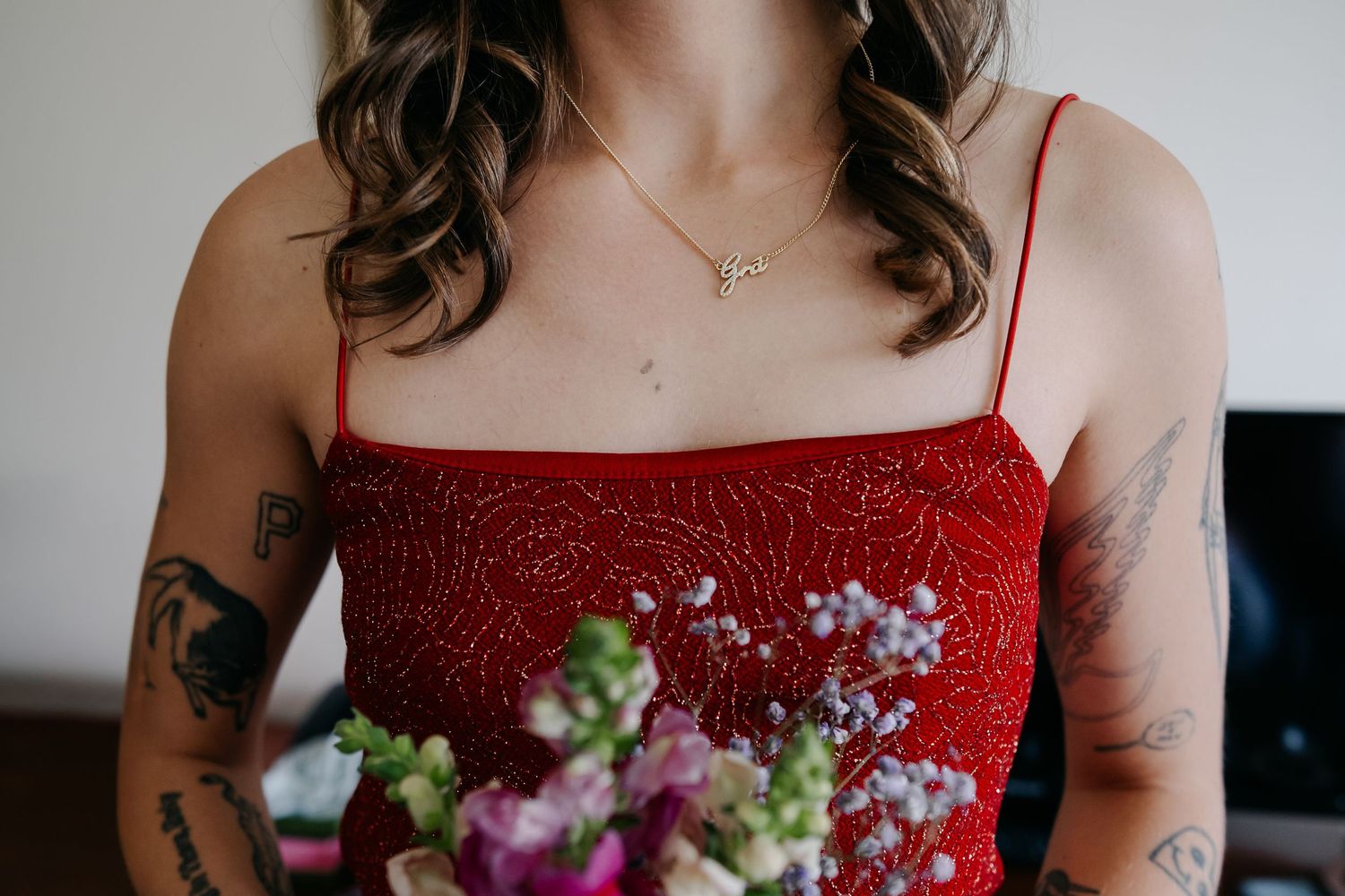 A person in a red sparkly dress holds a delicate bouquet of purple and white flowers against a light background.