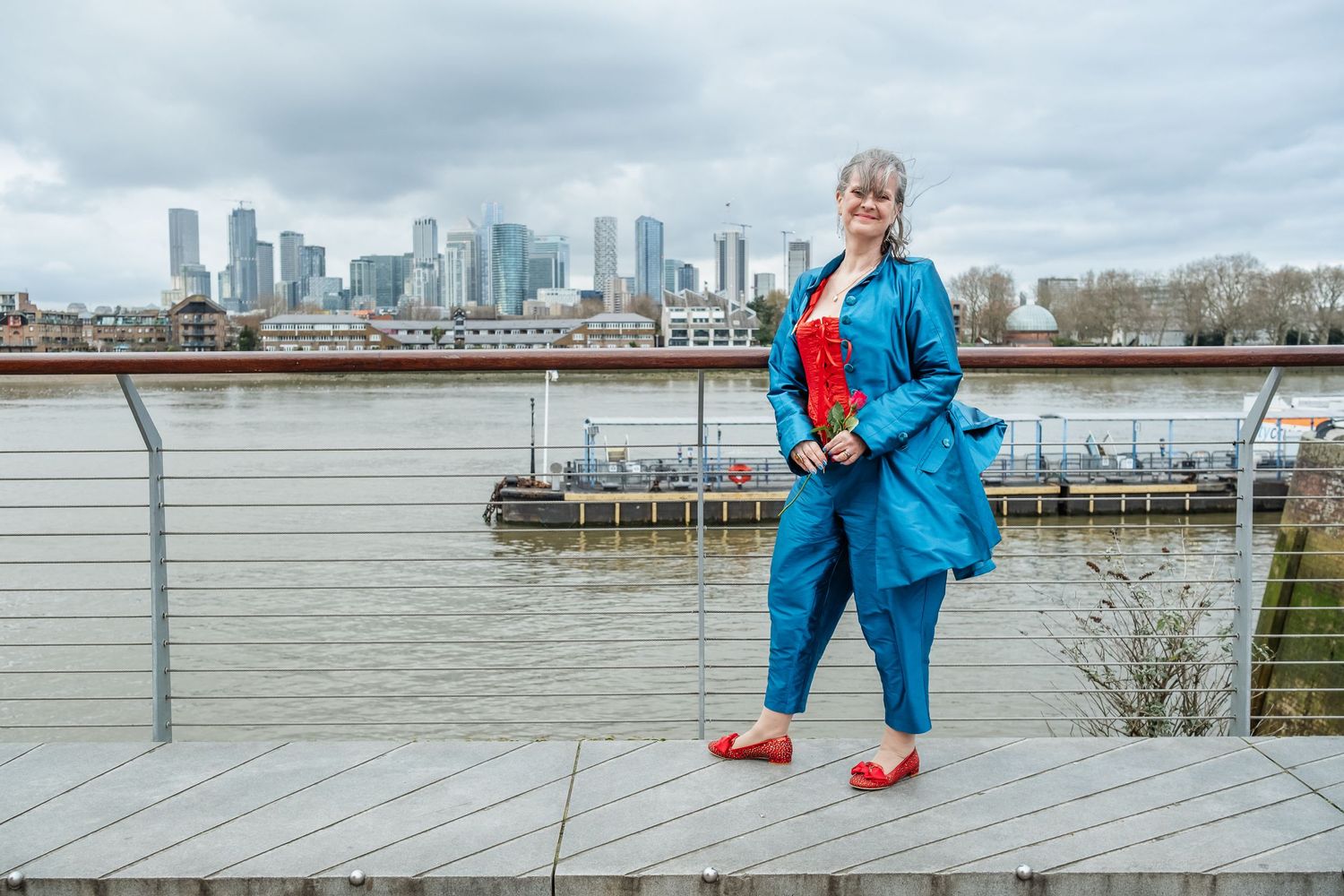 Person in bright blue suit poses on waterfront deck with city skyline in background.