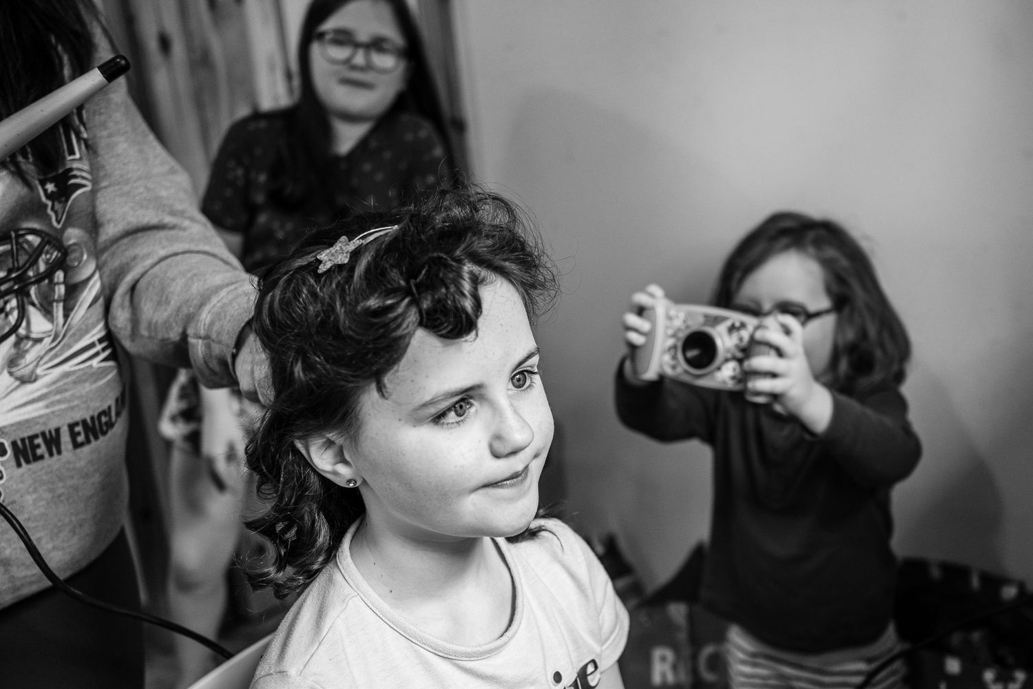 Person getting hair styled while another captures photo in background.