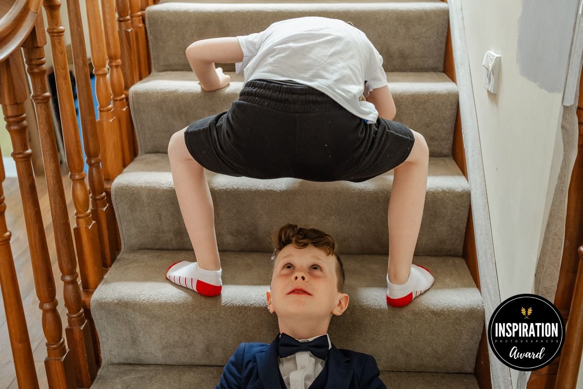 Young boy in black shorts and white shirt doing a handstand on carpeted stairs with wooden banisters.