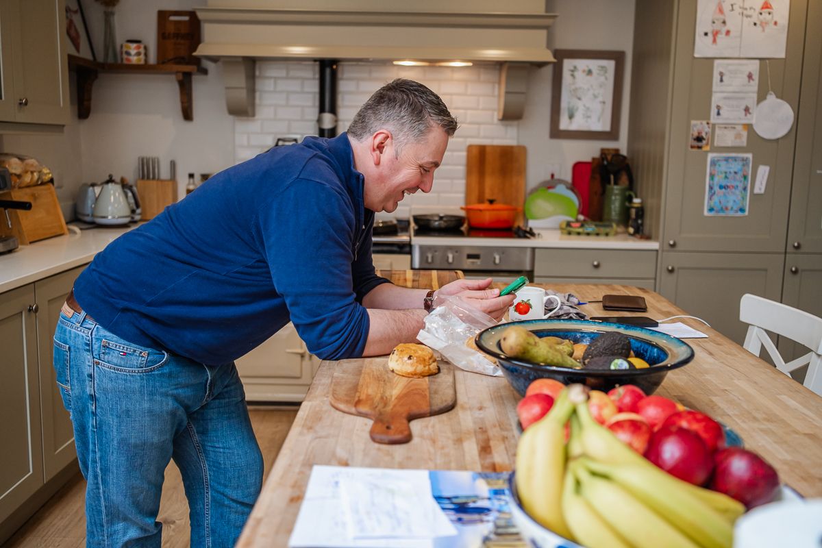 Man preparing food on a wooden kitchen island surrounded by fresh fruit and vegetables.