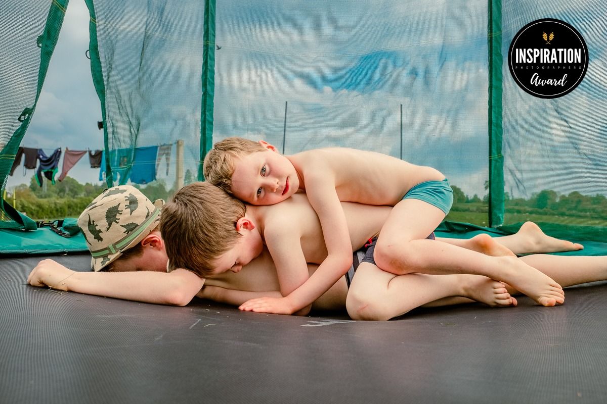 Two young children playfully wrestle and laugh together on a green mat during playtime.