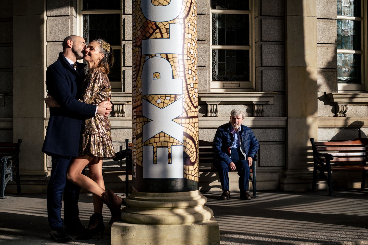 Couple embracing at National Library Dublin with a surprised onlooker in dramatic sunlight.