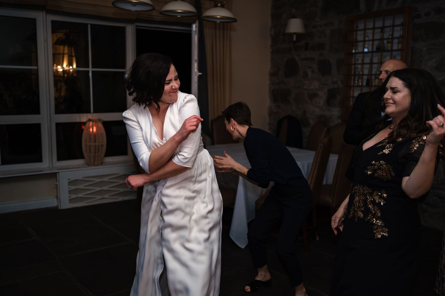 Bride in white dress dancing and laughing with guests at an elegant wedding reception venue.