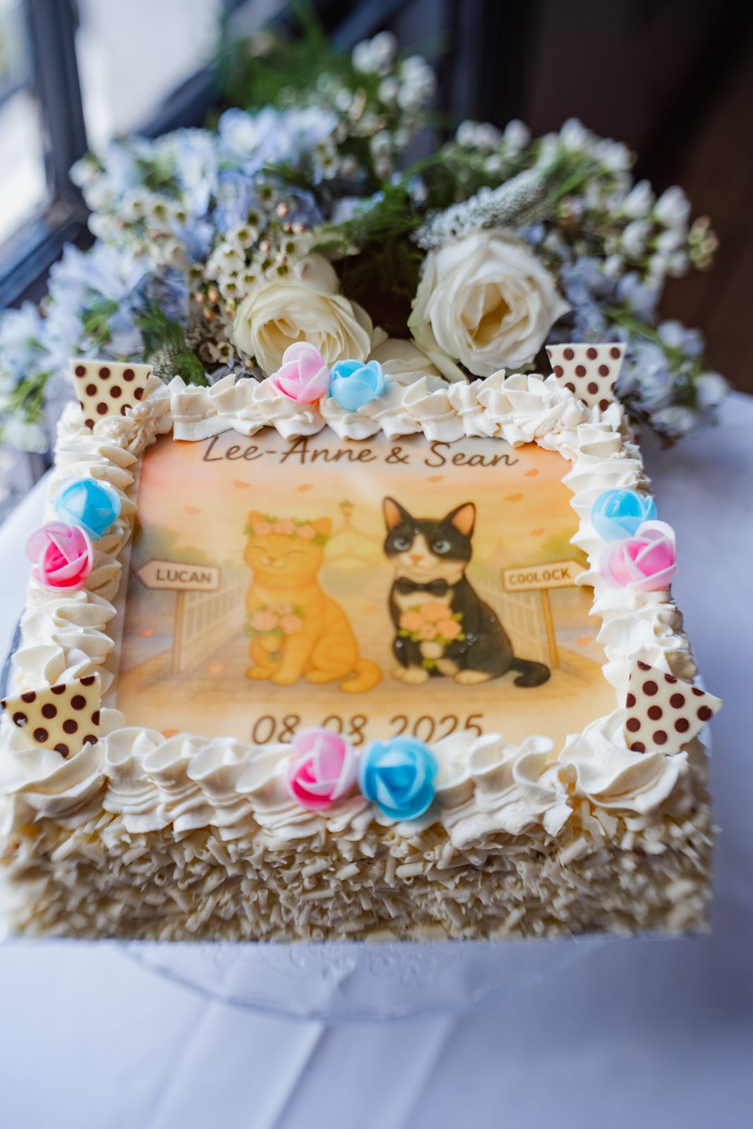 Wedding cake decorated with cat designs, roses, and personalized names in delicate frosting.