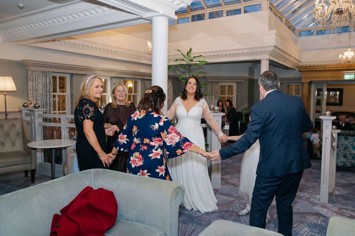 Bride in white gown greeting guests in elegant hotel lobby during wedding reception.