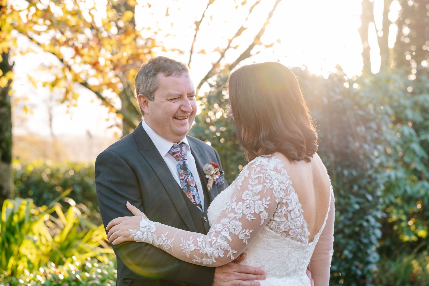 Bride and groom sharing a joyful moment outdoors during golden hour, with lush greenery and warm sunlight in the background.