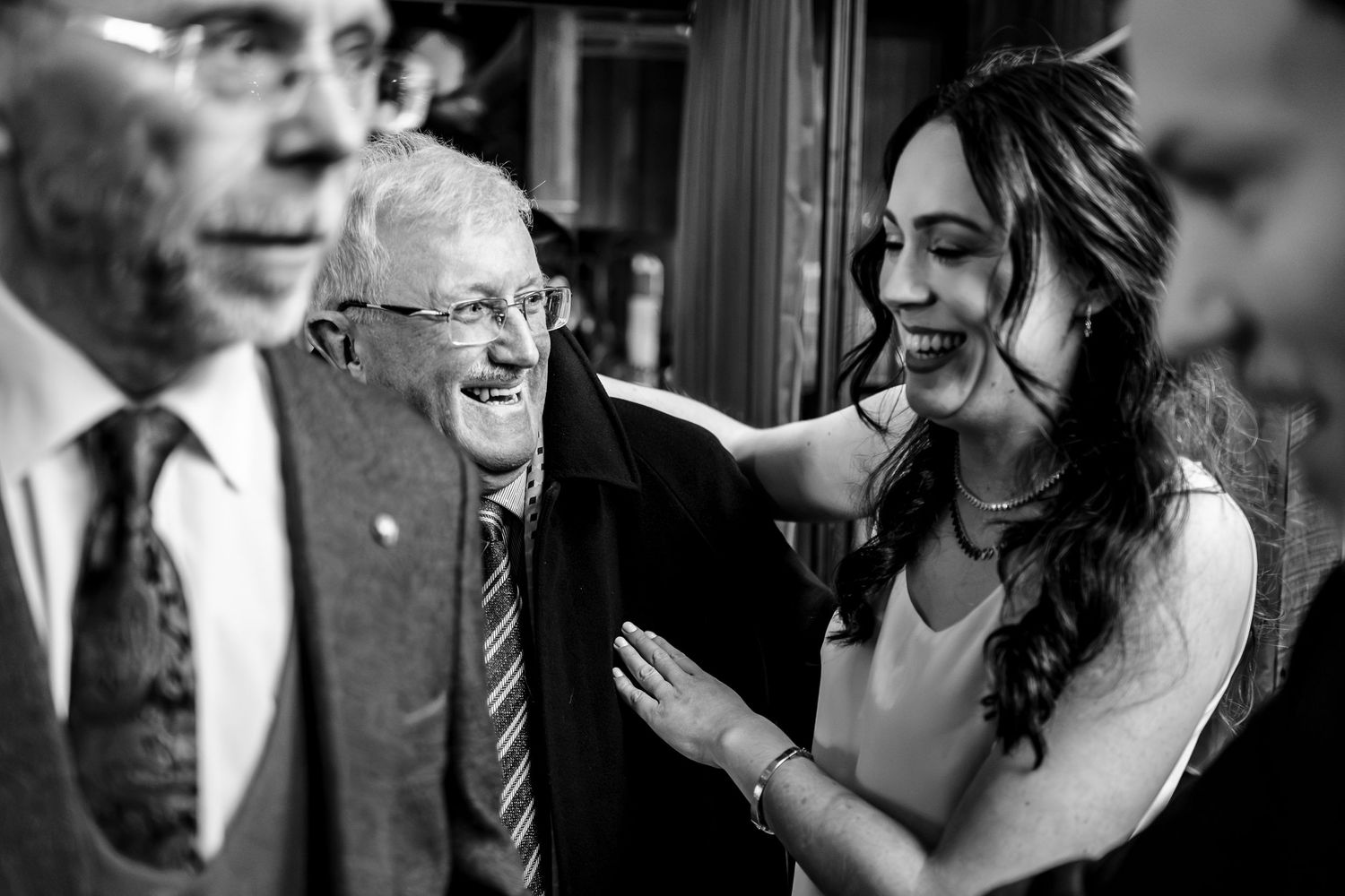 Black and white photo of elderly man smiling warmly as young woman places hand on his shoulder at a formal gathering.