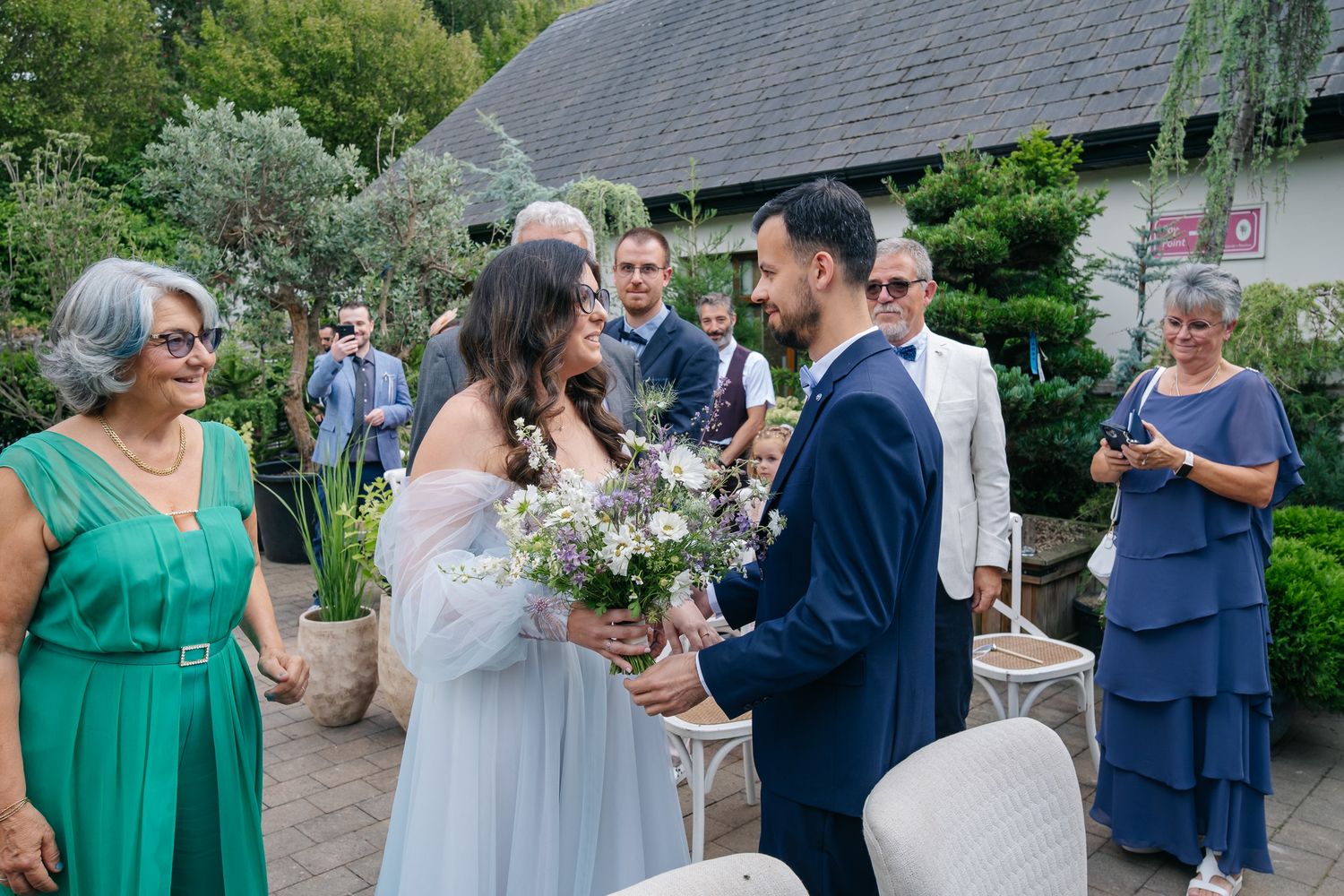 Bride and groom exchange smiles during outdoor wedding ceremony surrounded by guests in elegant attire.