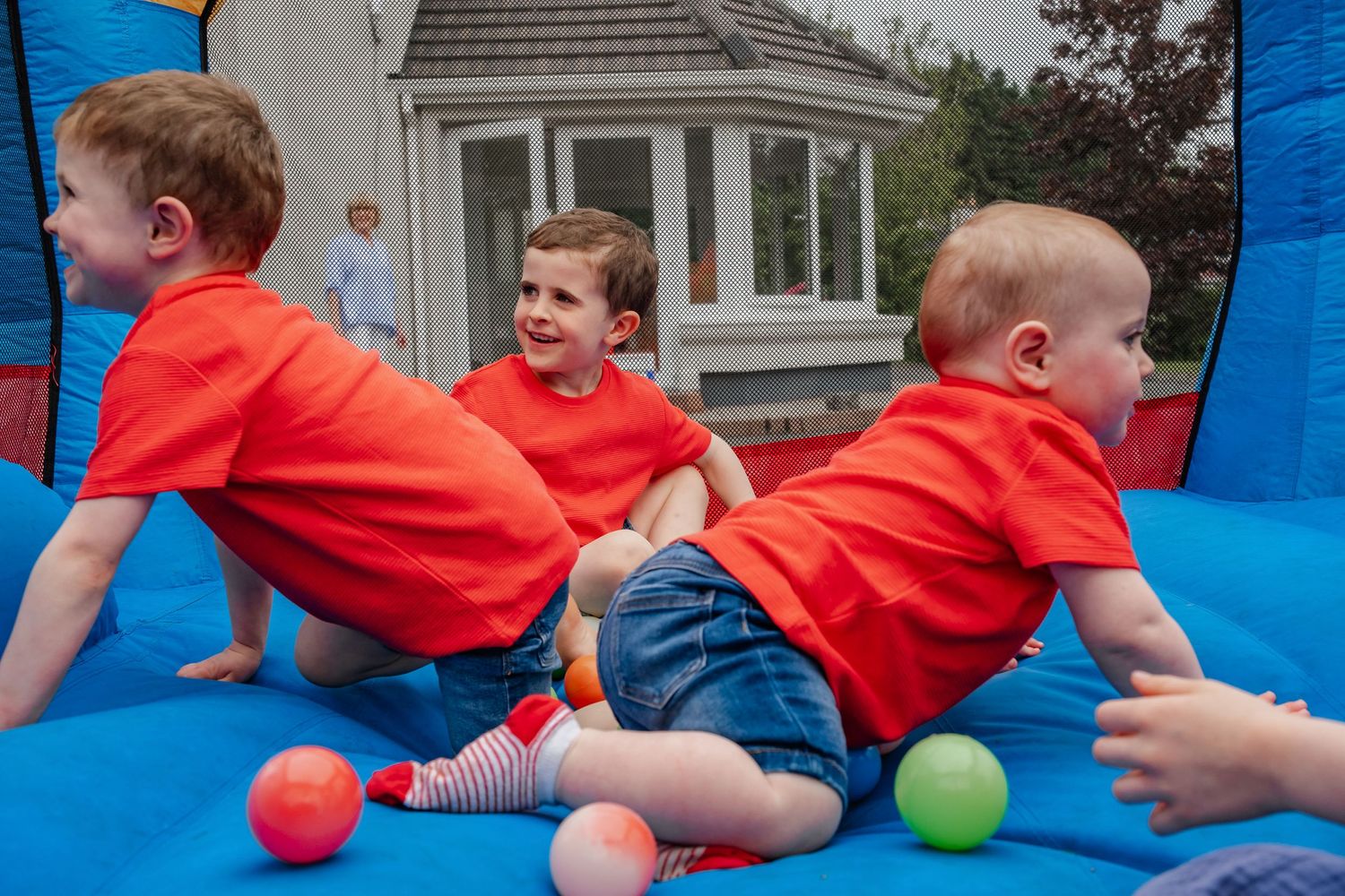 Children in red shirts playing with colorful balls in blue bounce house.