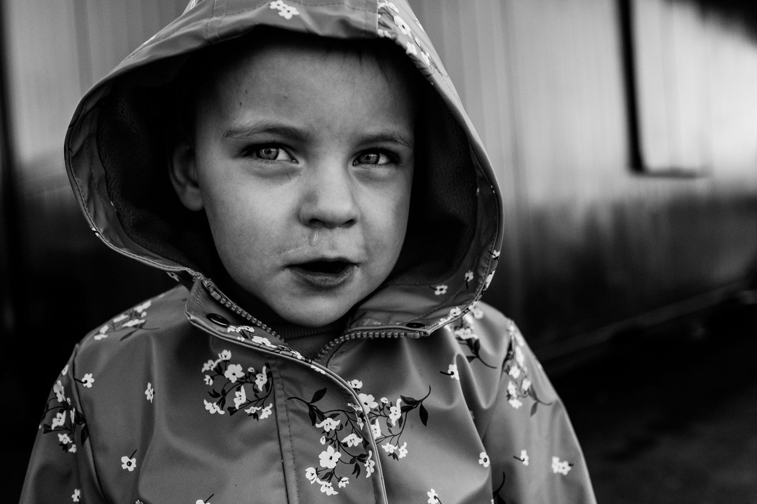Black and white portrait of a child wearing a hooded raincoat with floral pattern.