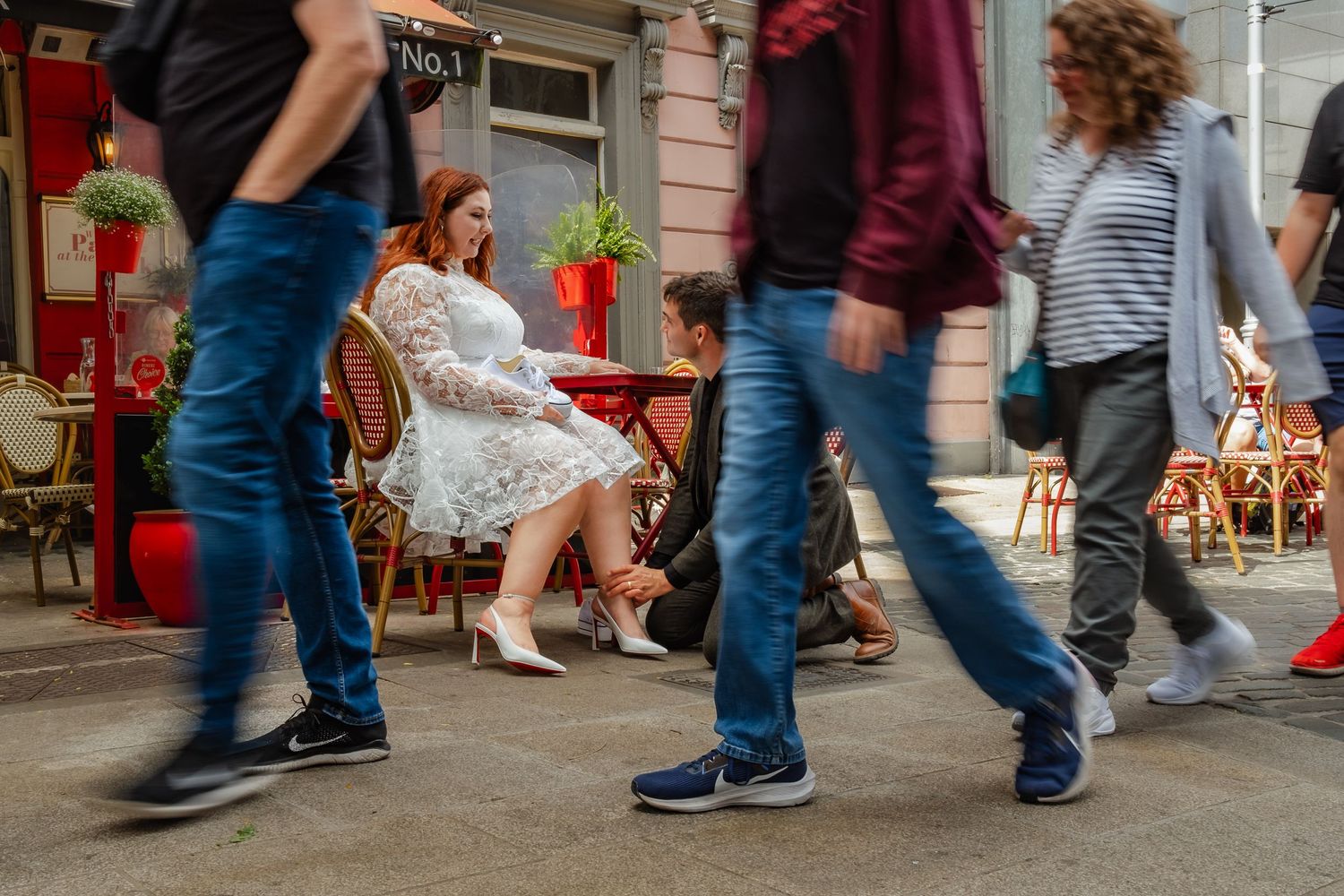 A busy street scene with pedestrians walking past a cafe with red outdoor seating.