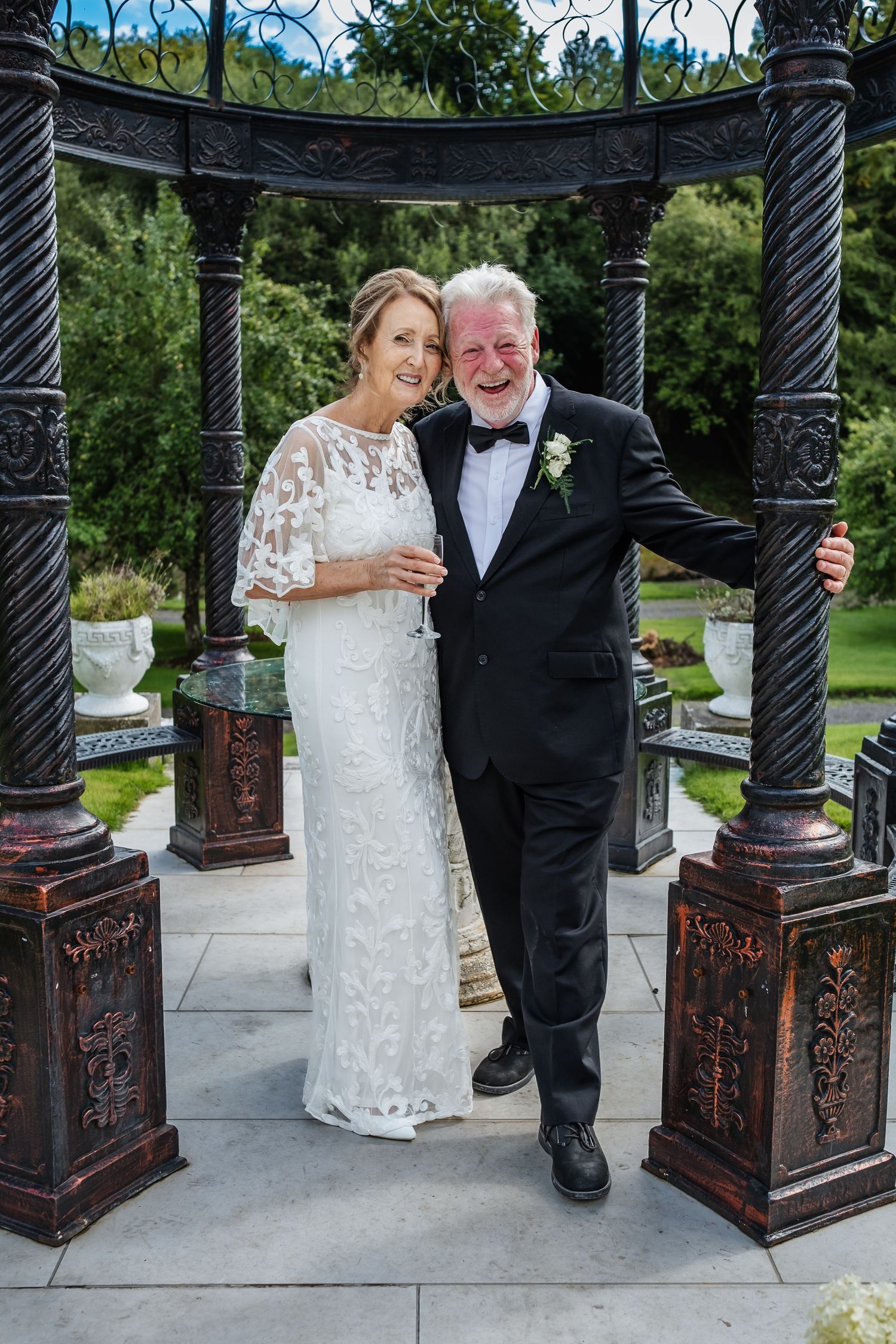 Elegant wedding photo in ornate black gazebo with decorative iron details.