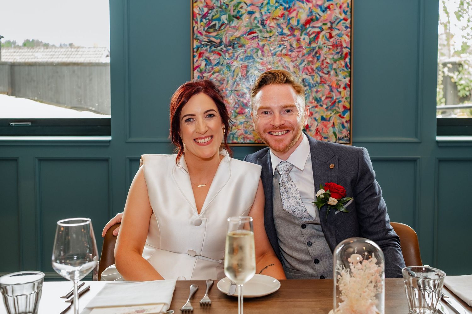 Wedding guests seated at tables in restaurant dining room with colorful floral wallpaper and white table settings.