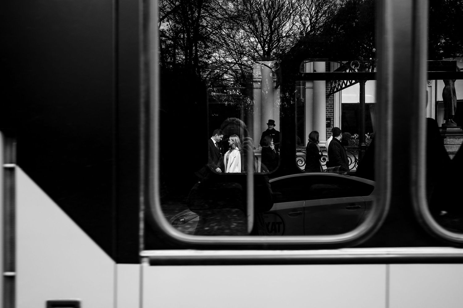 Black and white photo of a couple seen through a bus window.